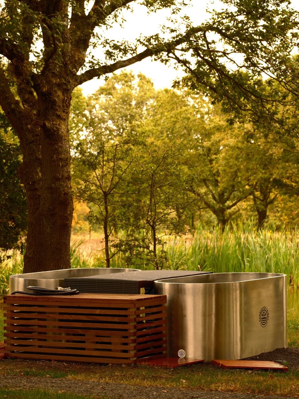 Two stainless steel ice baths in an outdoor setting next to a lake