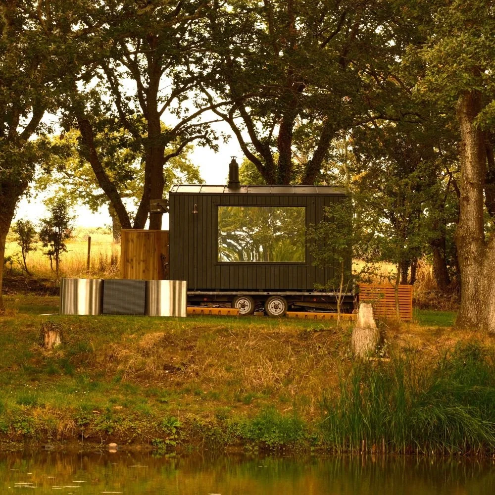 An outdoor wooden sauna hut with steel ice baths in front in a woodland setting