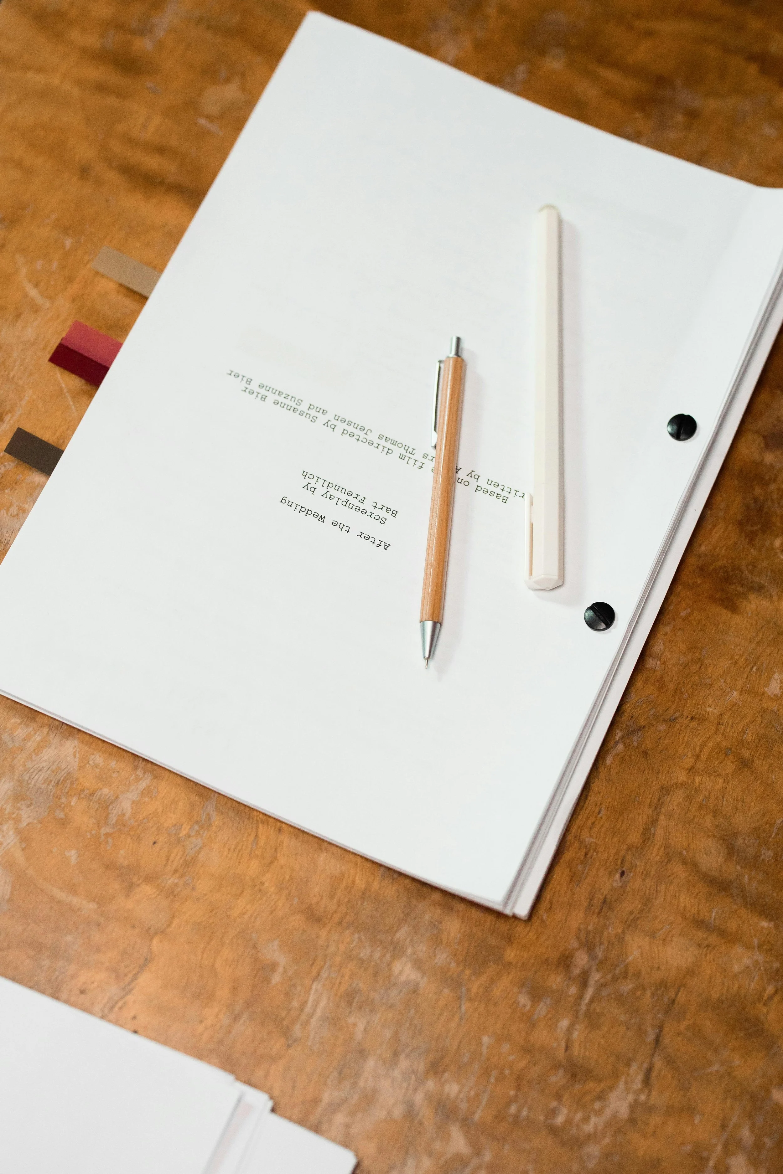 Close-up of a white file folder with a typed document, a beige pen, and a translucent white ruler on a wooden surface.
