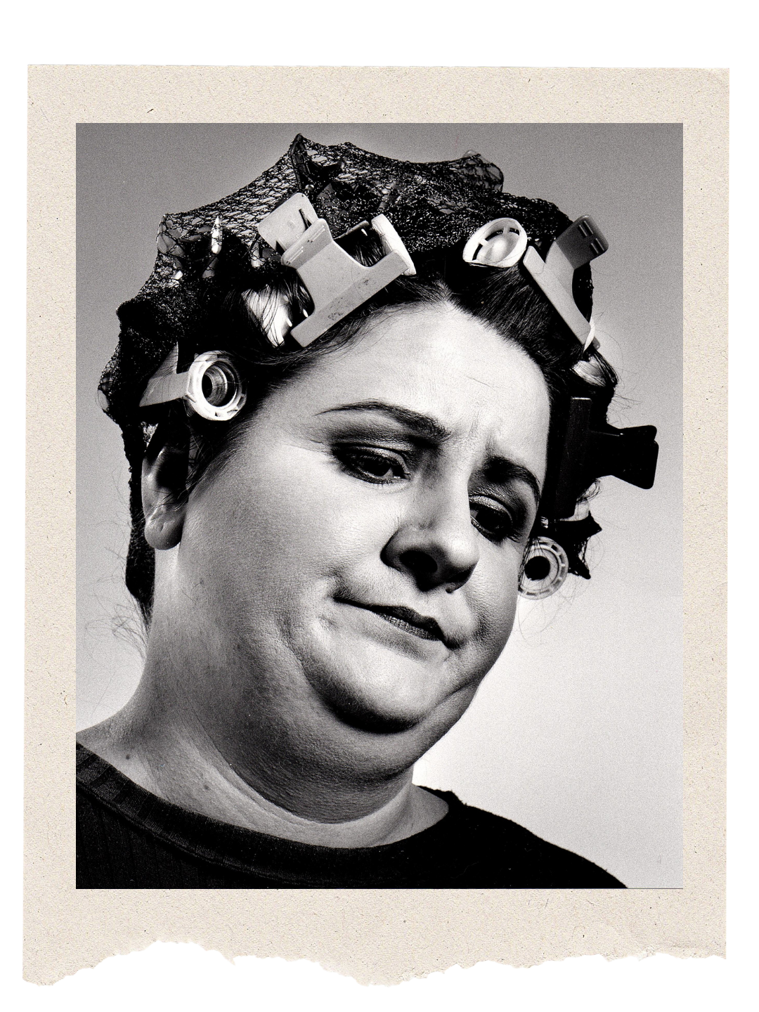 Sara Ford A black and white close-up portrait of a woman with hair rollers and curlers in her hair, making a sad or disappointed expression.