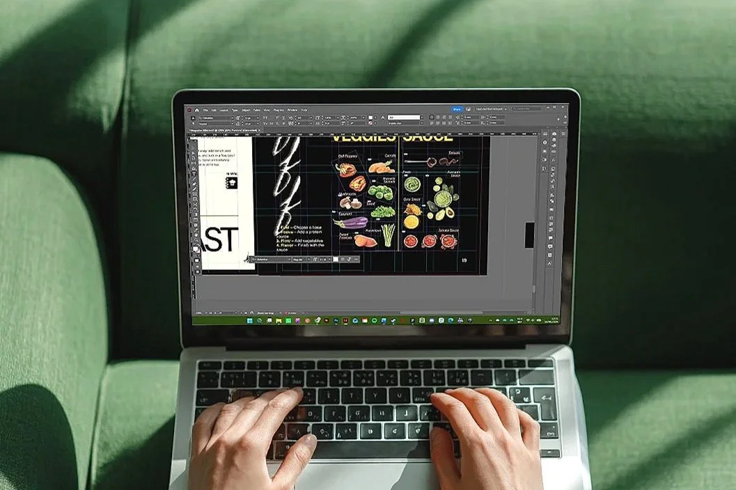 Persoon bewerkt een menu voor een restaurantsaus op een laptop in een groene zithoek.