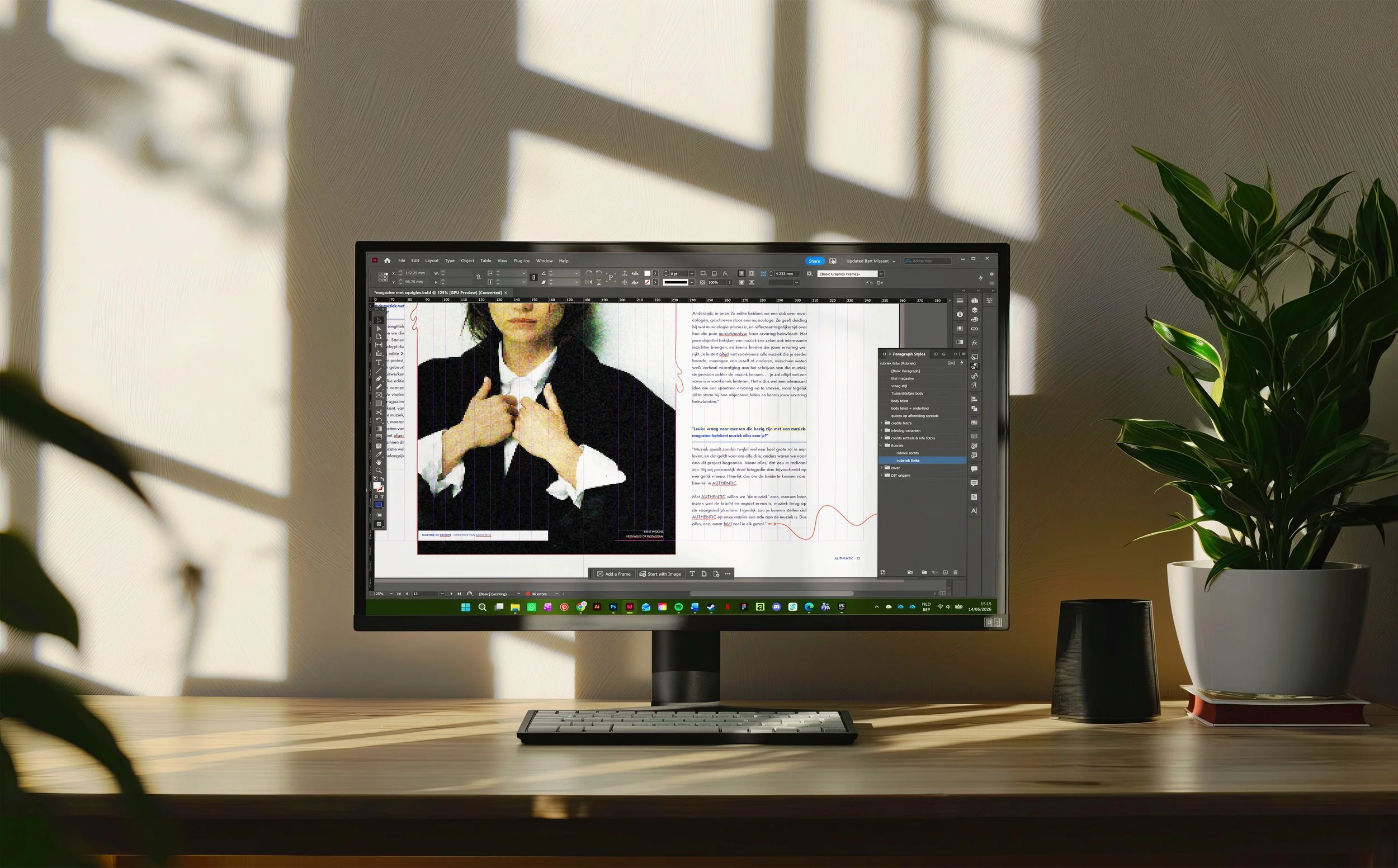 Een computermonitor op een houten bureau met een toetsenbord, dat een grafisch ontwerpprogramma toont met een afbeelding van een vrouw in een donkere jas en witte blouse. Er staan twee kamerplanten naast de monitor.