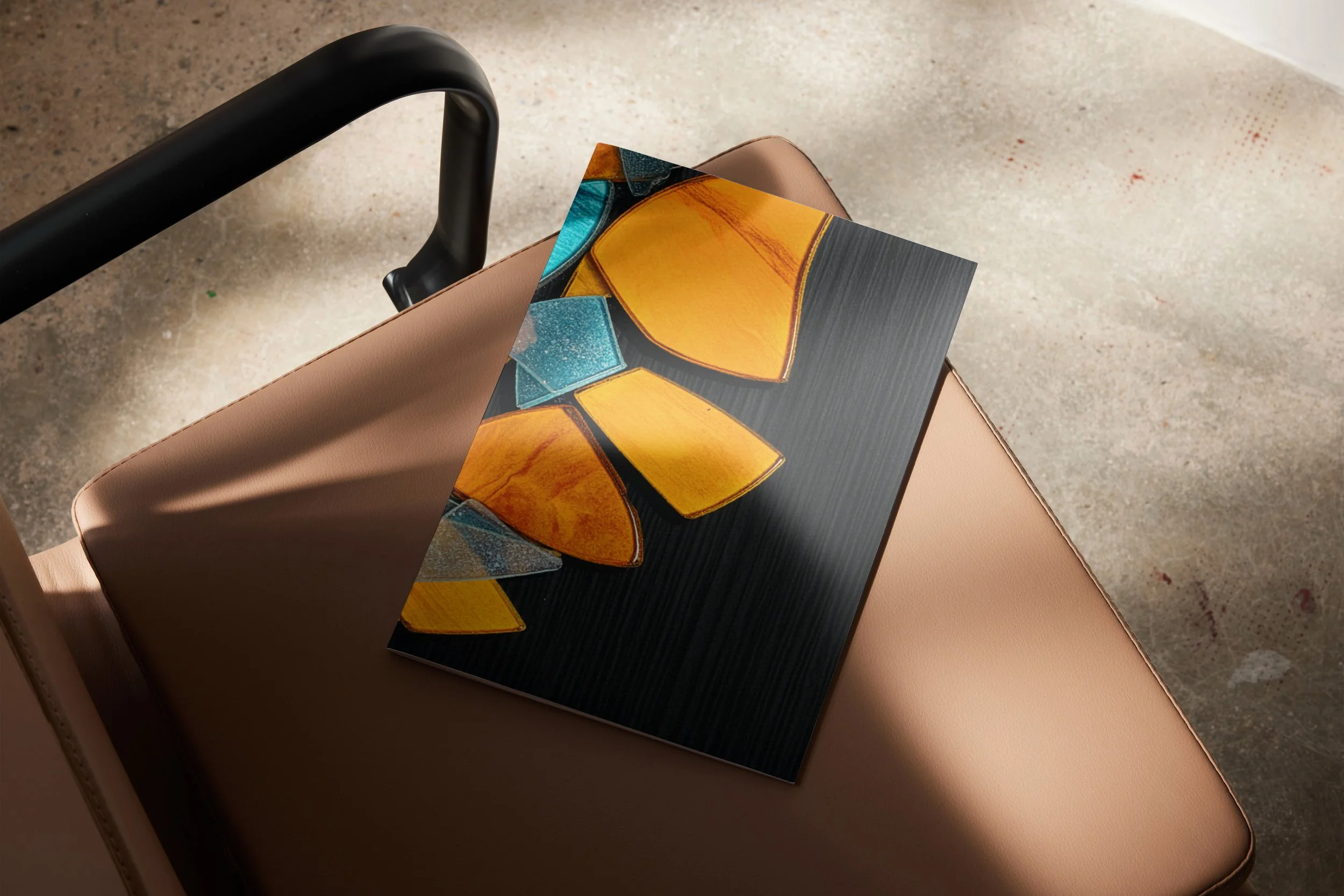 Een stoel met een beige bekleding en een zwarte armleuning, met een kunstboek op de zitting die een kleurrijk abstract ontwerp toont, in een ruimte met gepolijst betonnen vloer.
