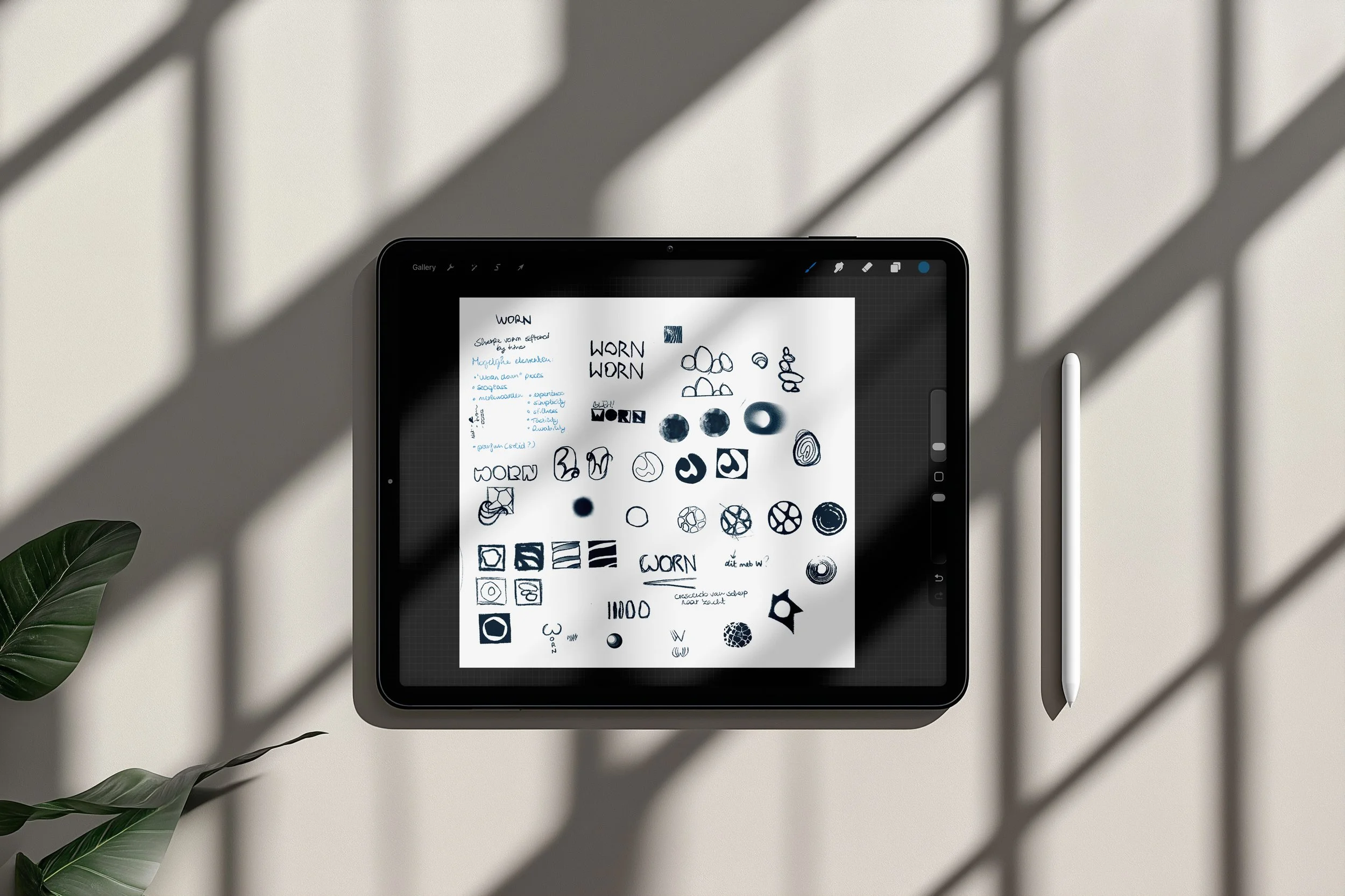 Een tablet met een styluspen, waarop schetsen en ontwerpen van logo's staan, ligt op een lichte tafel met schaduwpatronen. Naast de tablet liggen groene bladeren.