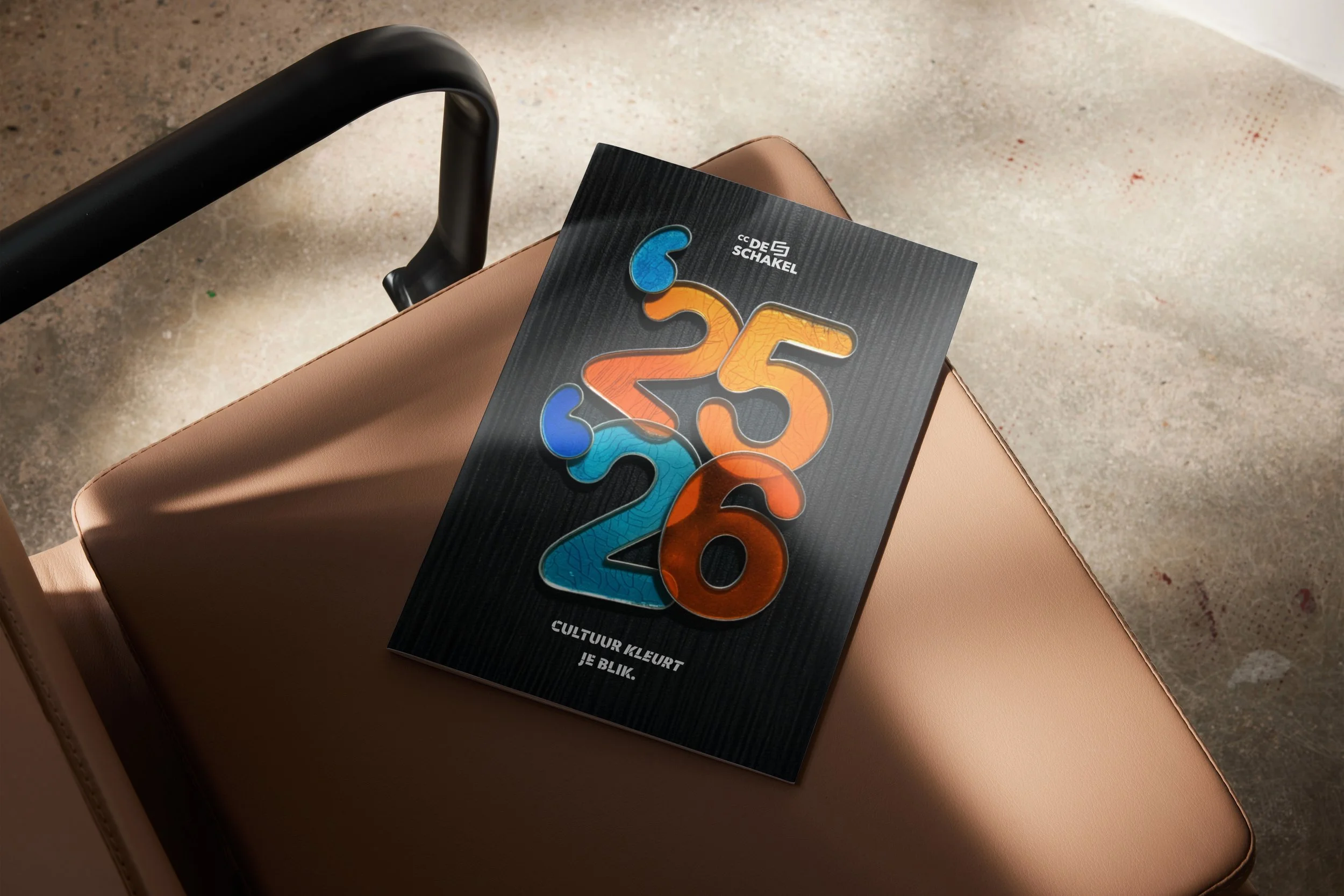 Een brochure met kleurrijke uitgesneden cijfers ligt op een beige stoel.