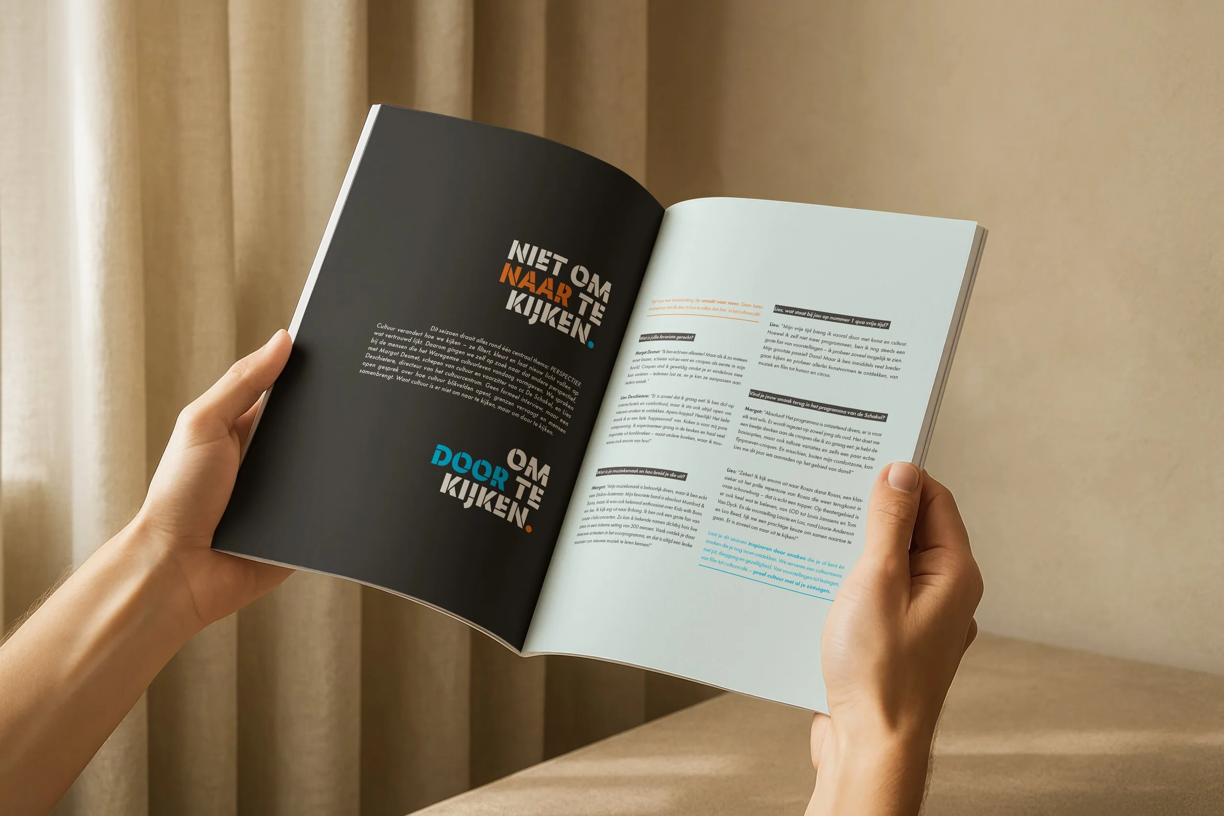 Een persoon houdt een open magazine vast dat in een kamer met beige gordijnen ligt.