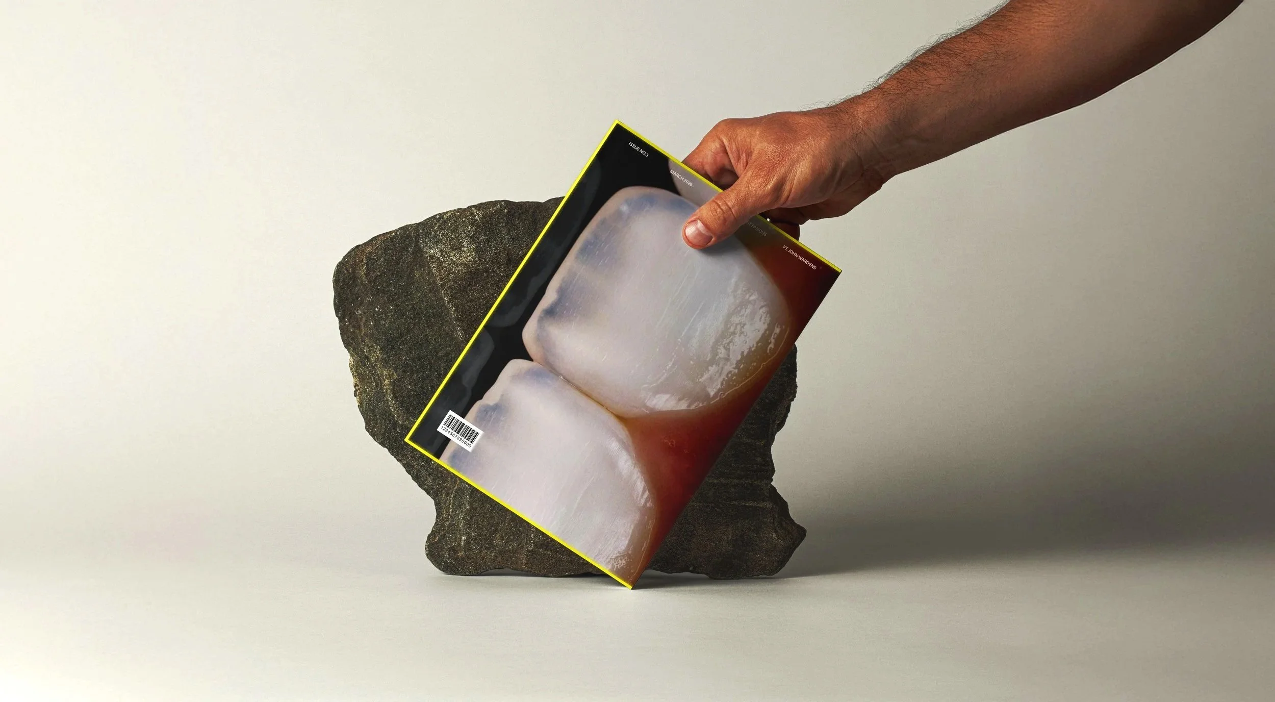 Hand houdt een magazine vast dat in contact komt met een rots, terwijl de achtergrond wit is.