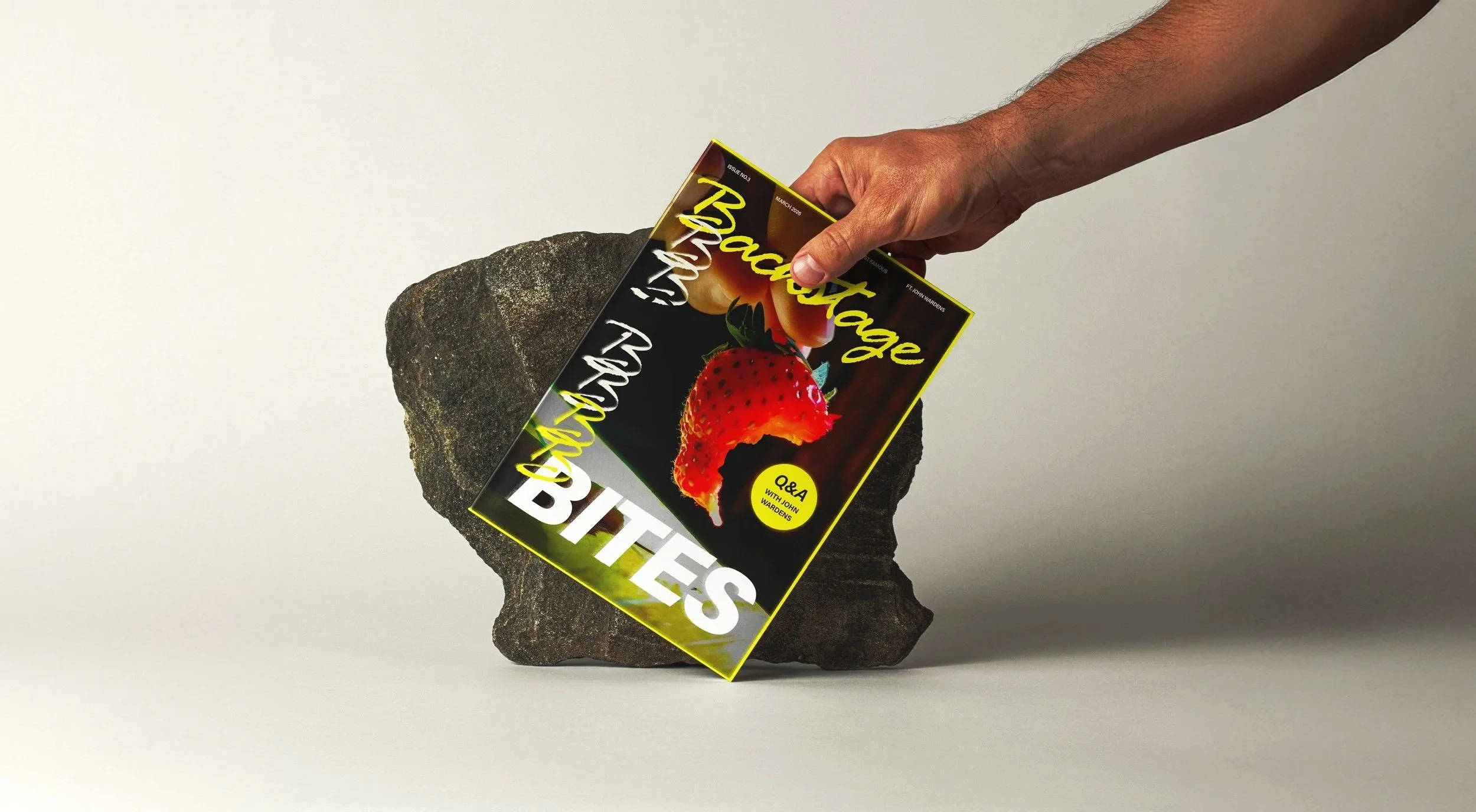 Mensenhand die een magazine vasthoudt boven een rots, met een lege muur op de achtergrond.