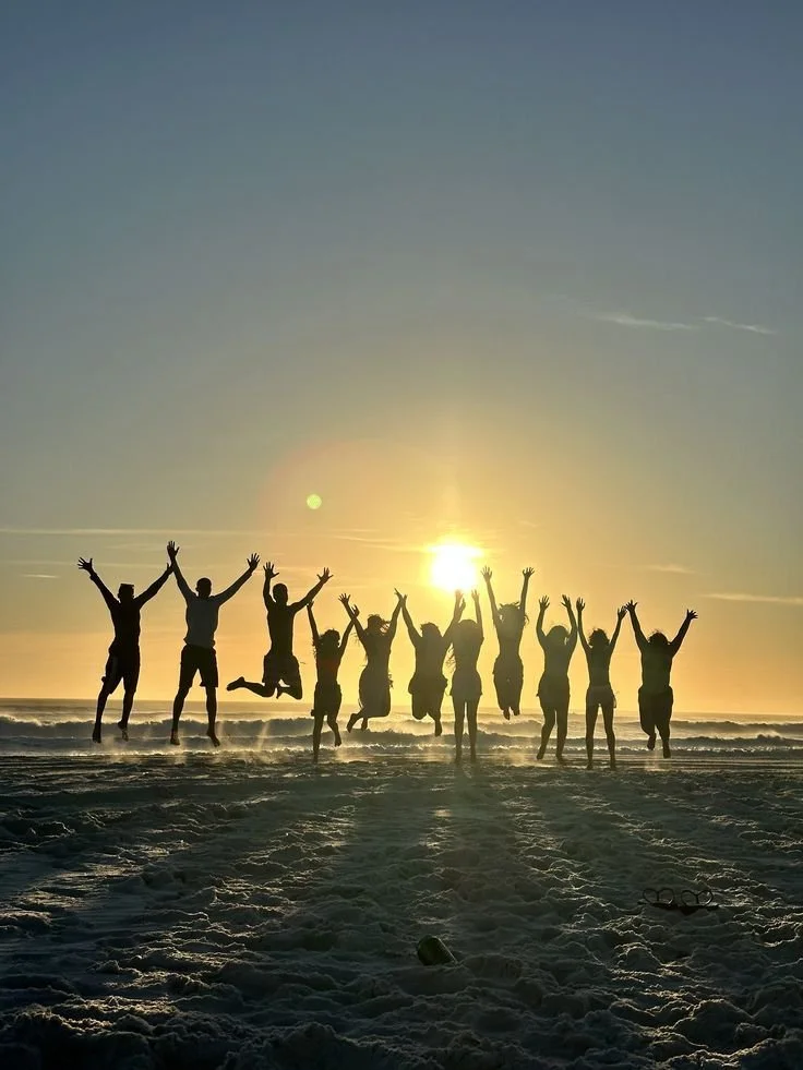 Group of people jumping in the air on a sandy beach at sunset.