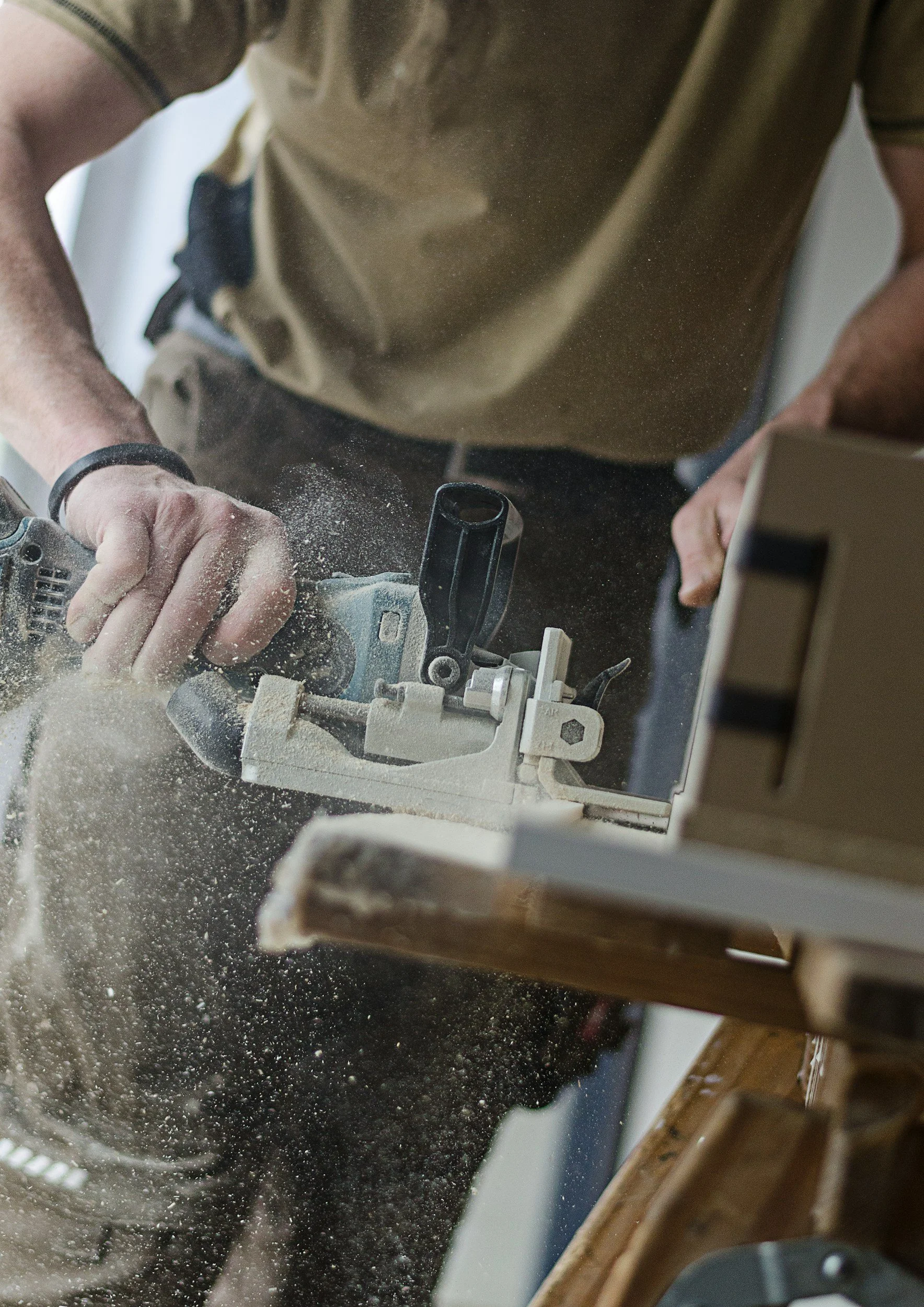 Close-up of a person using a jigsaw to cut wood, with sawdust flying in the air.