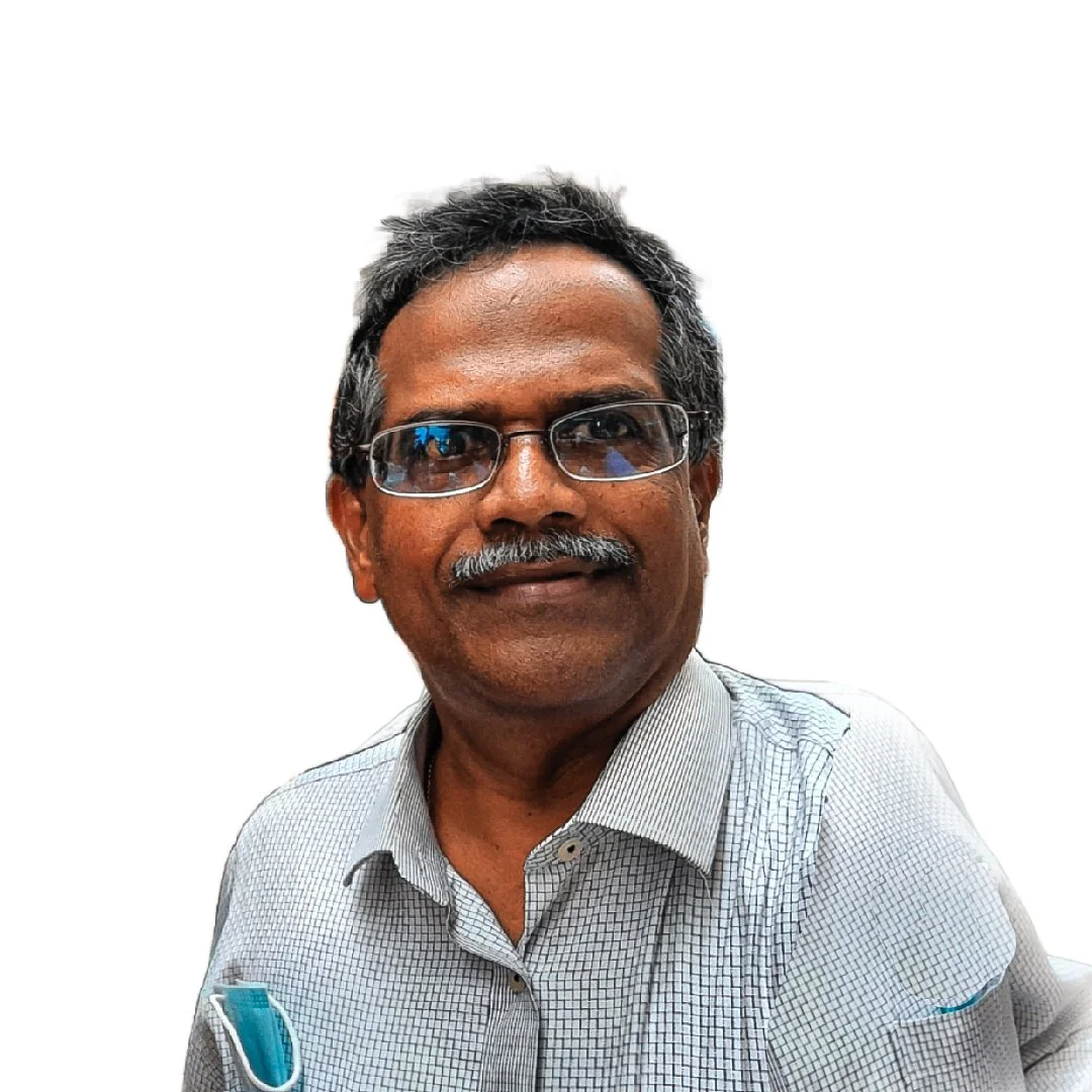 A middle-aged man with dark hair and a mustache, wearing glasses and a checked shirt, standing against a plain white background.