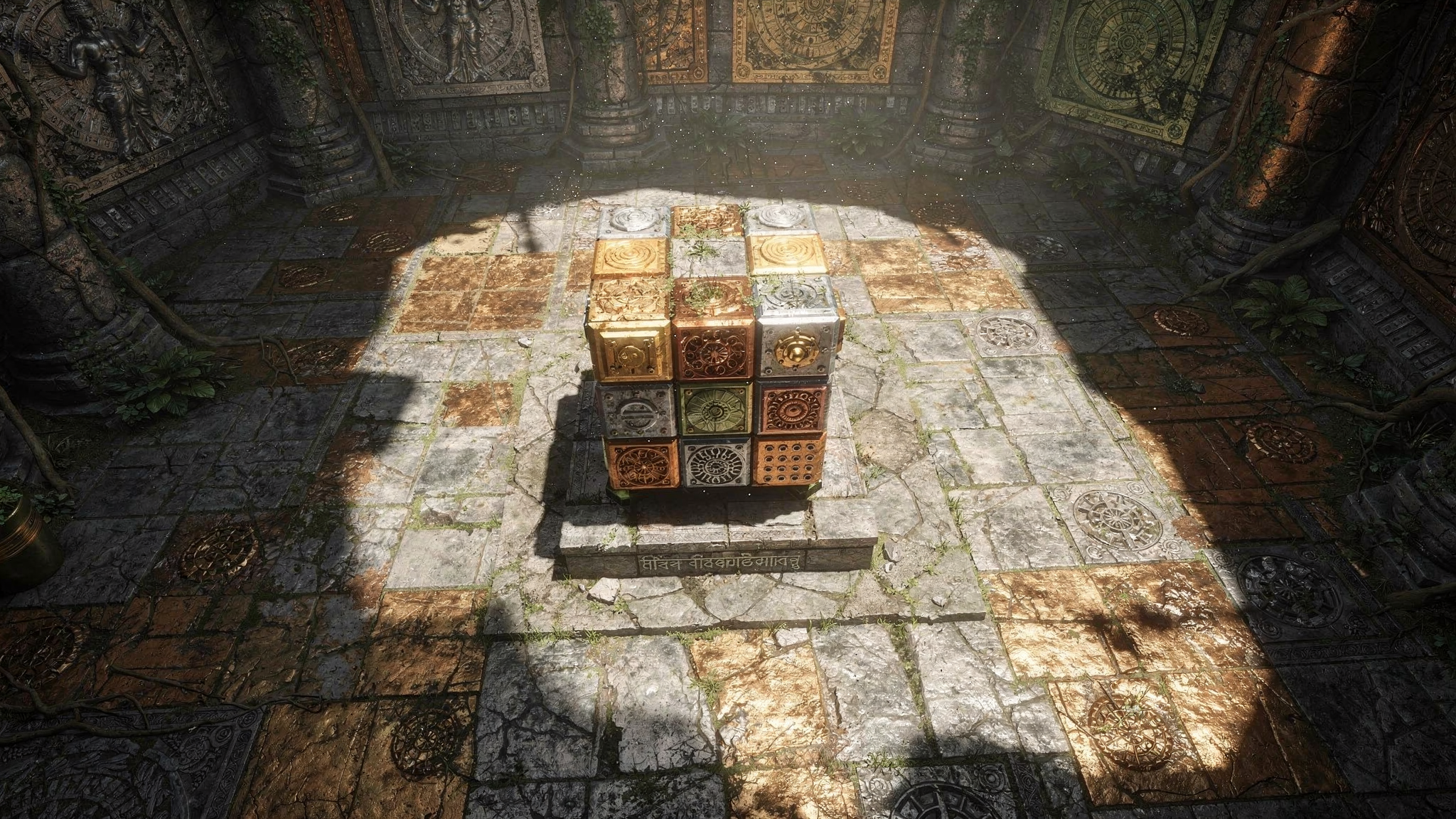A small Rubiks Cube of decorative ceramic tiles with intricate patterns in gold, bronze, and silver, placed on a stone pedestal in an ancient ruin or temple with stone walls and floor, some greenery, and traditional carvings.