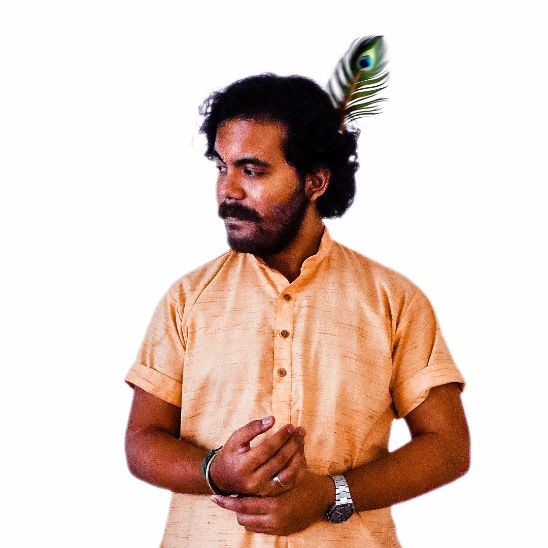 A man with dark hair and a beard wearing an orange kurta, looking to his left, with a peacock feather tucked into his hair.