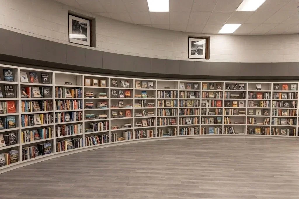 Curved white bookshelves filled with books in a library or bookstore, with framed pictures hanging on the wall above.
