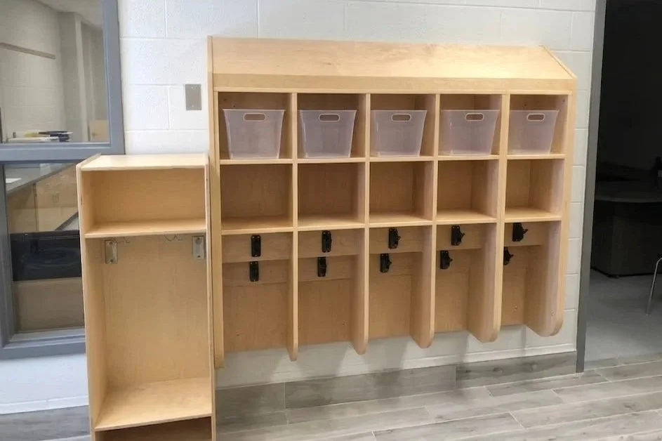 Wooden cubbies with clear plastic bins and hooks for organizing shoes and belongings in a school or daycare setting.