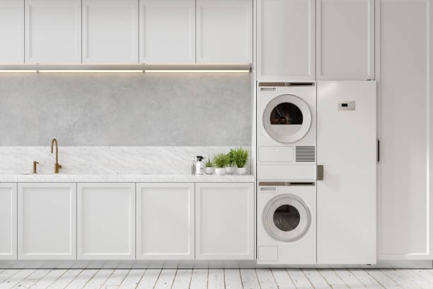 A modern laundry room with white cabinets, a marble countertop, a gold faucet, and a stacked washer and dryer unit.