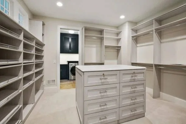 Empty walk-in closet with built-in shelves, drawers, and hanging rods, and a laundry room with a washer and dryer visible through an open door.