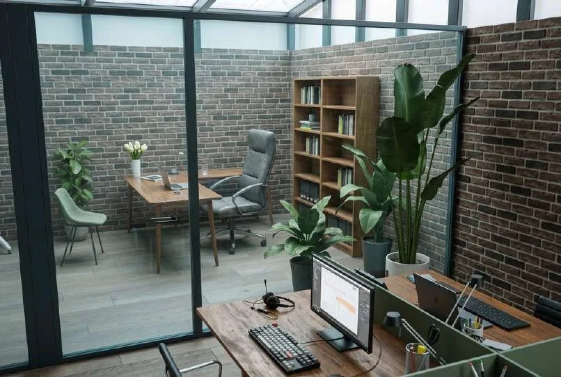 Bureaux modernes avec plusieurs ordinateurs, plantes vertes, étagère en bois, mur en briques, et décoration de bureau élégante.