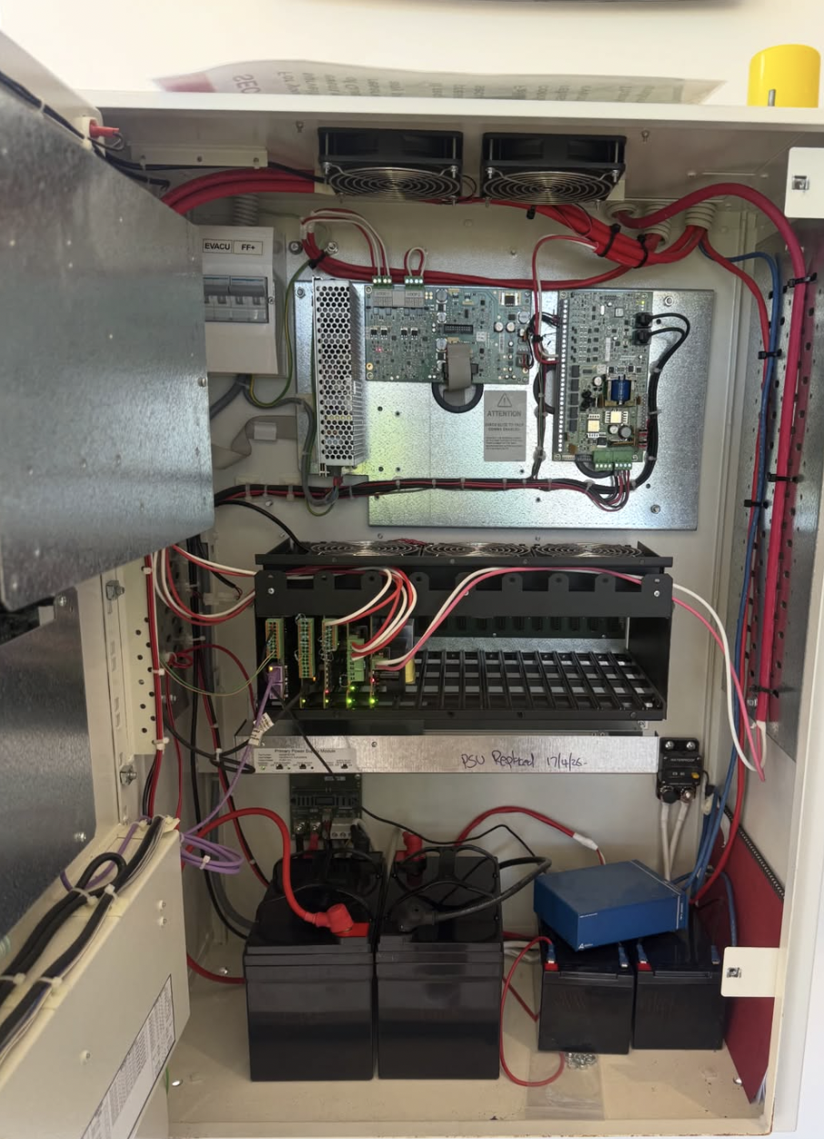 Inside an electrical control panel with various electronic components, circuit boards, wiring, and batteries.