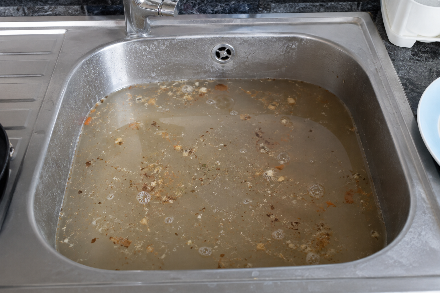 Dirty kitchen sink with leftover food and water.