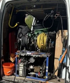 Equipment and tools inside the back of a service vehicle, including hoses, a reel, and a bucket.