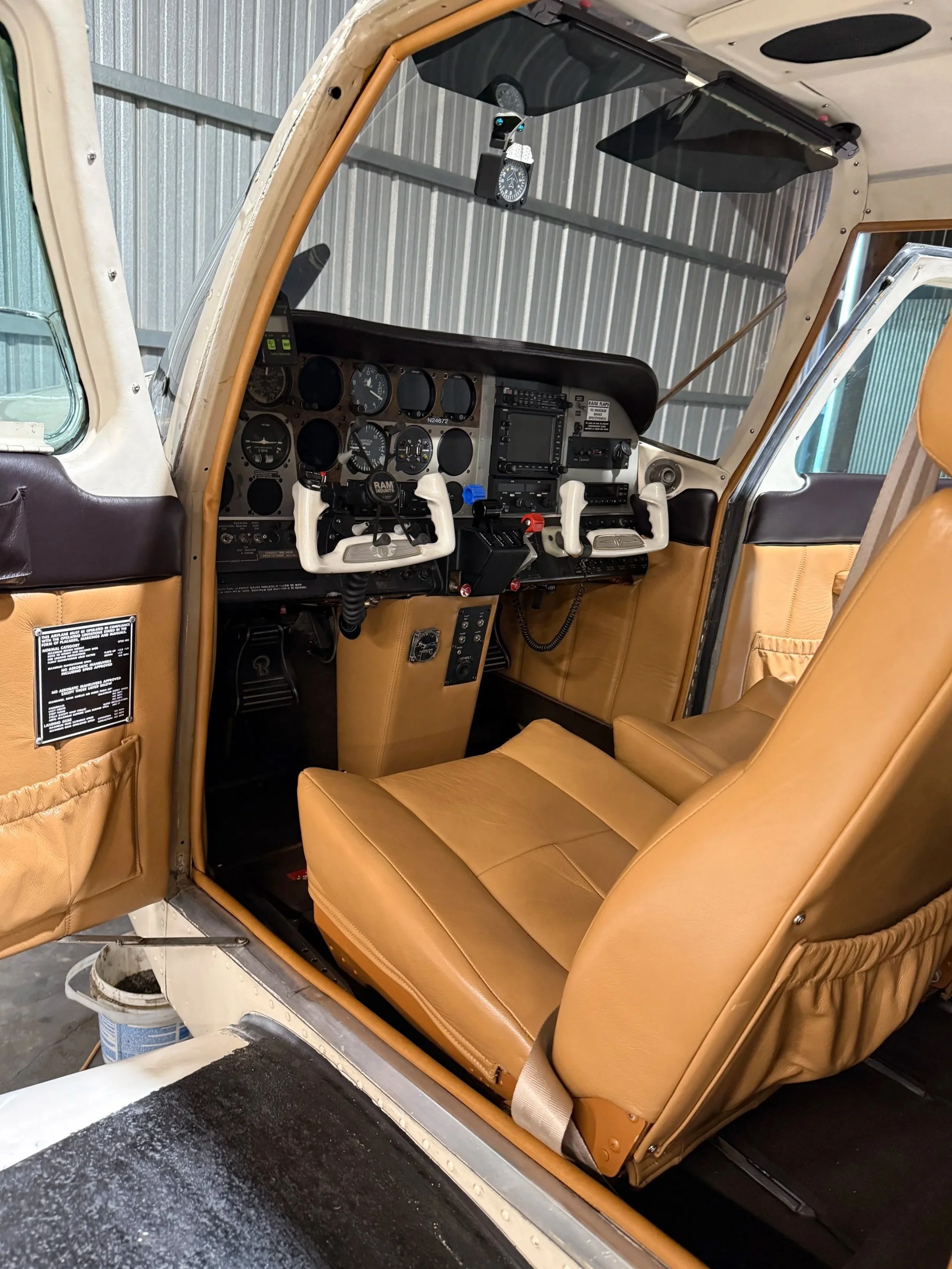 Interior of a small aircraft cockpit with tan leather seats, multiple dials, and controls on the instrument panel, and a propeller visible through the window.