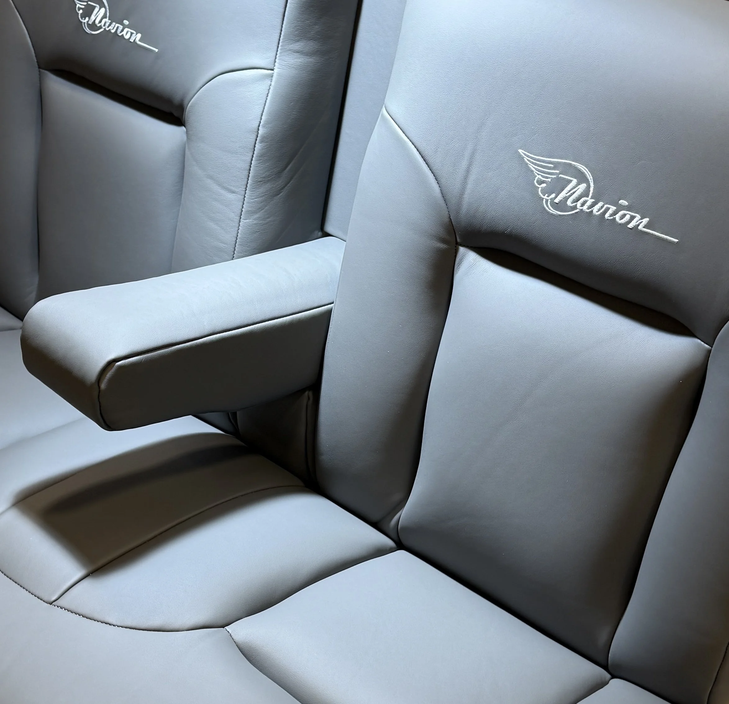 Close-up view of light gray leather car seats with embroidered logos, showing detailed stitching and modern design.