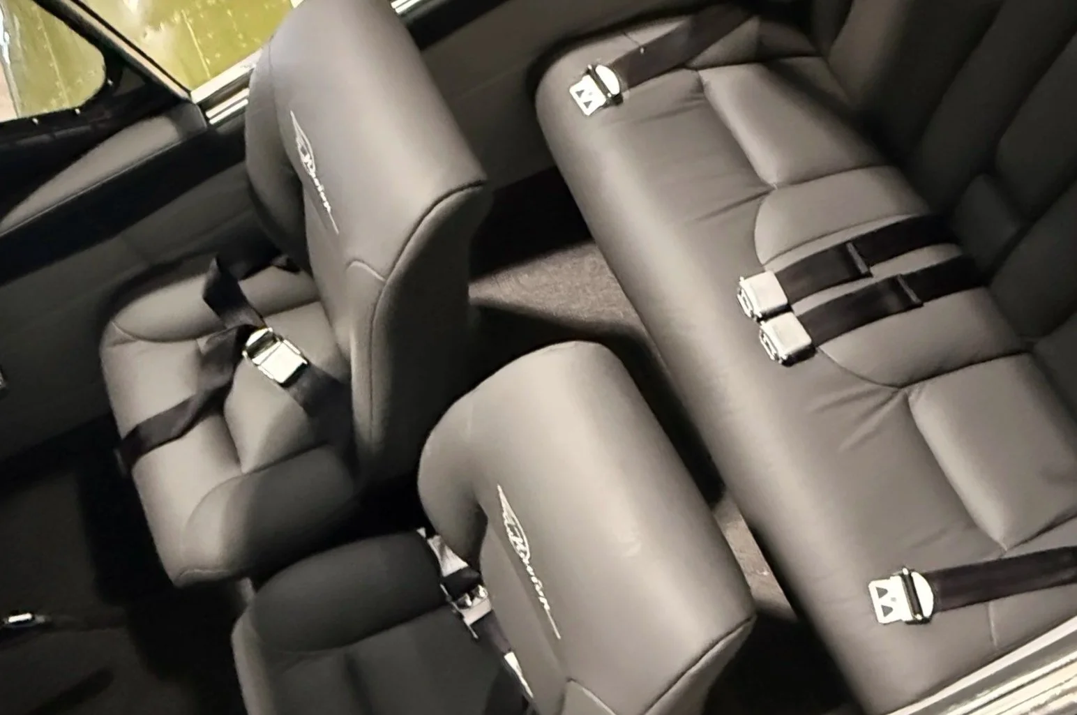 The inside of a vehicle showing two rear seats with black leather upholstery and seat belts.