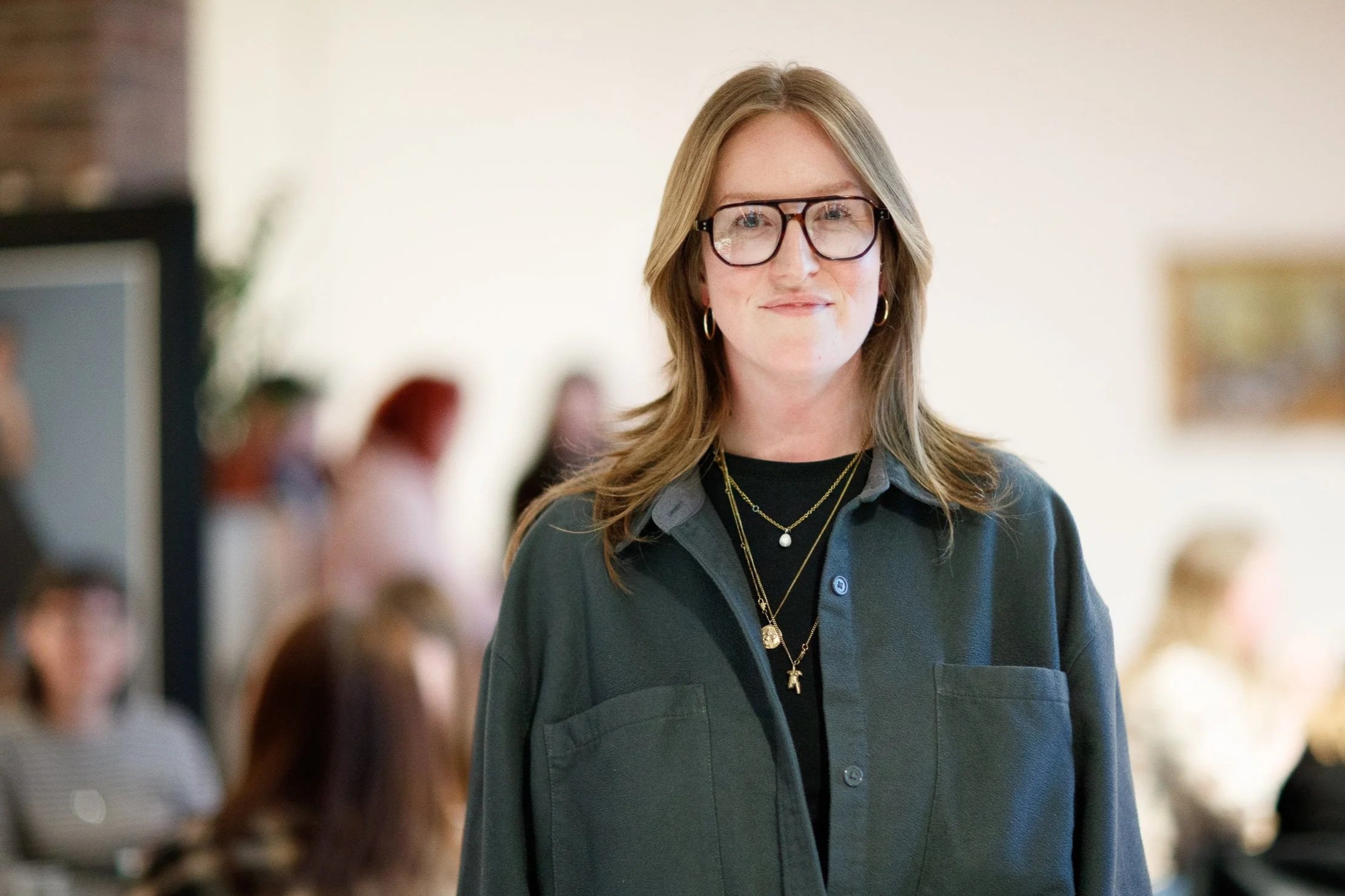 Cleo Goodman at a workshop, she is a white woman with fair, auburn hair, wearing glasses and a dark jacket. Participants are visible in the background.