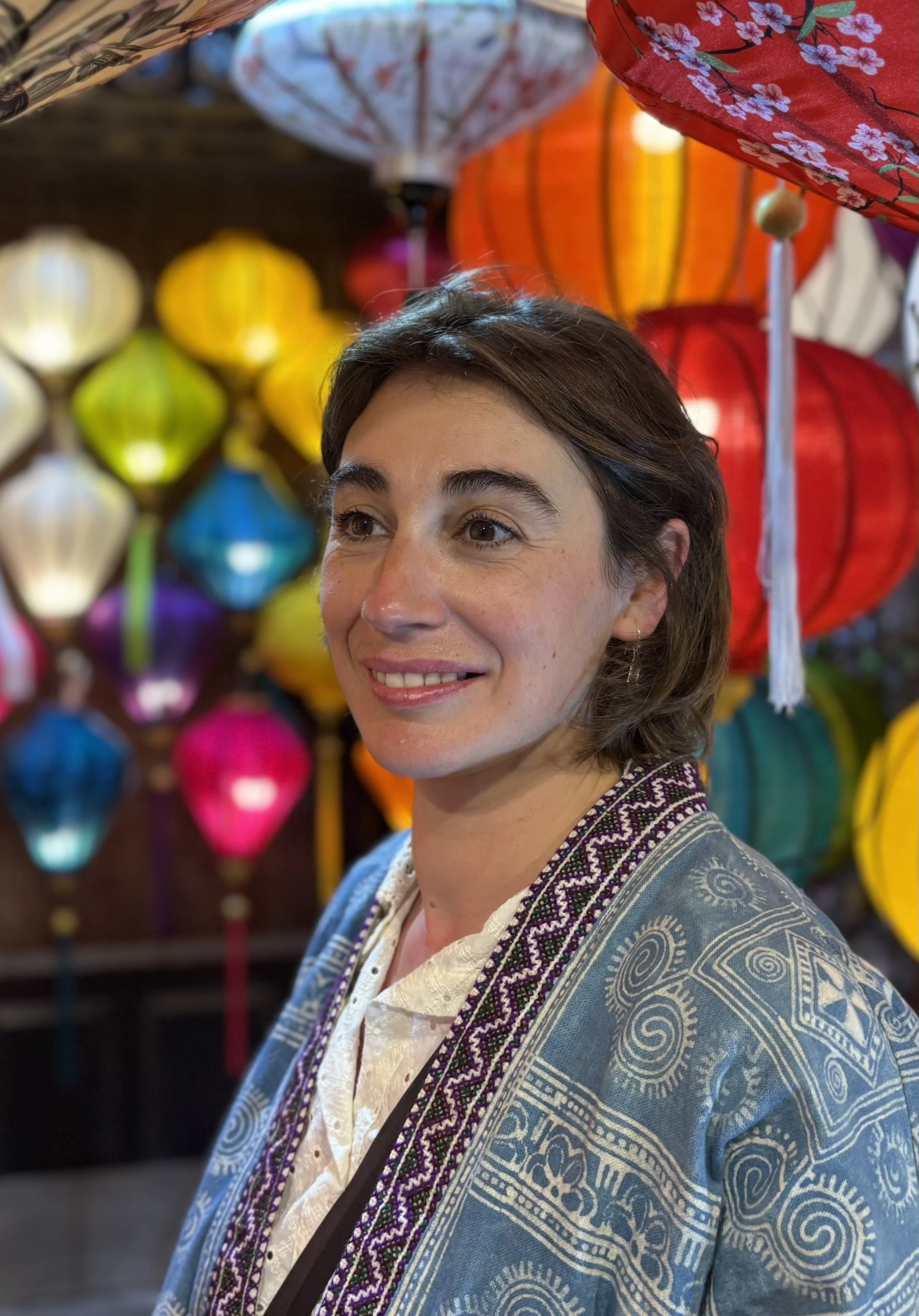 Eine lachende Frau in traditioneller Kleidung vor bunten Laternen bei einem asiatischen Festival.