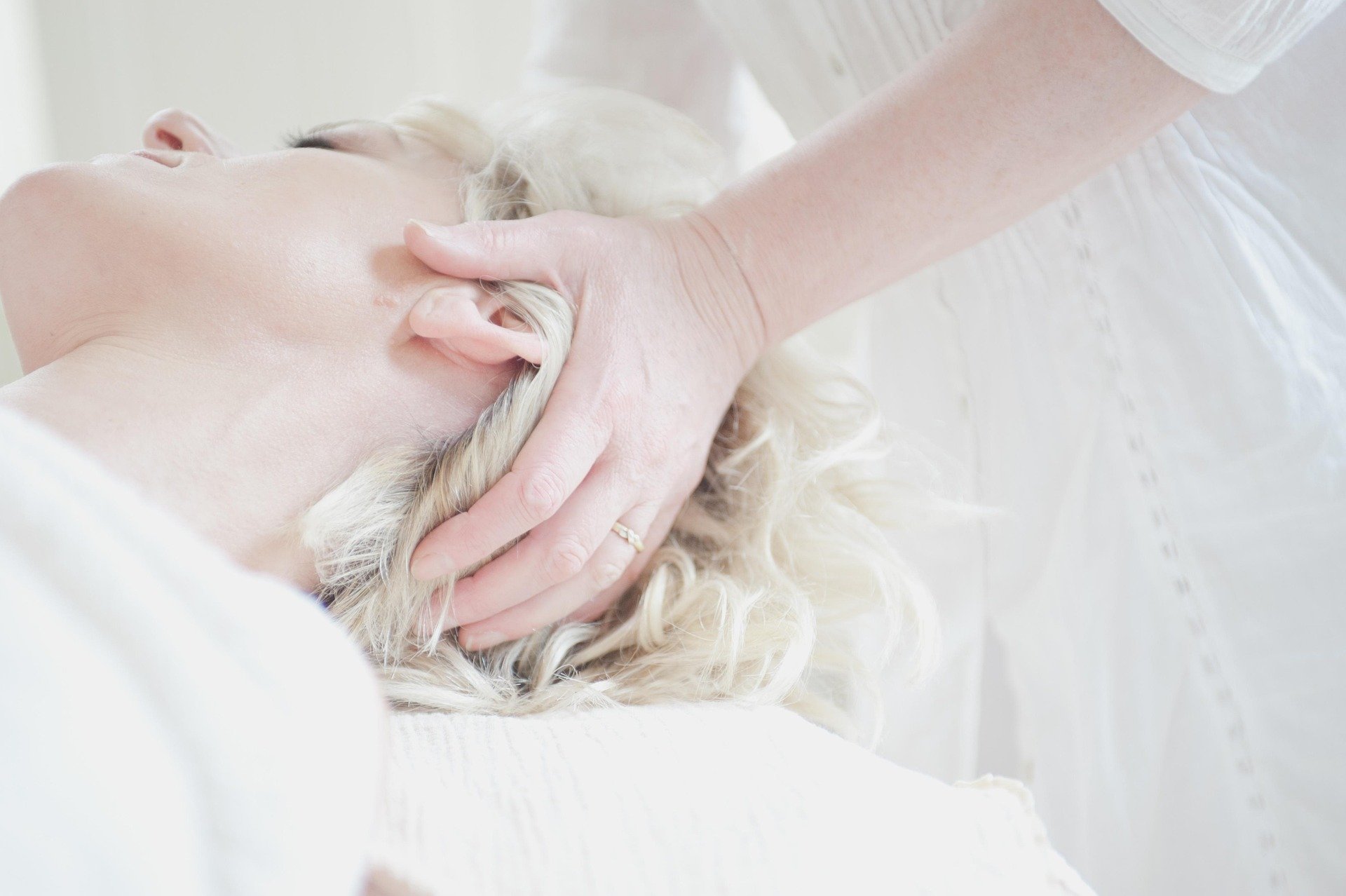 Person receiving a head massage or chiropractic adjustment on a woman with long blonde curly hair, lying peacefully on a massage table.
