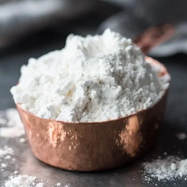A copper measuring cup filled with white flour on a dark surface.