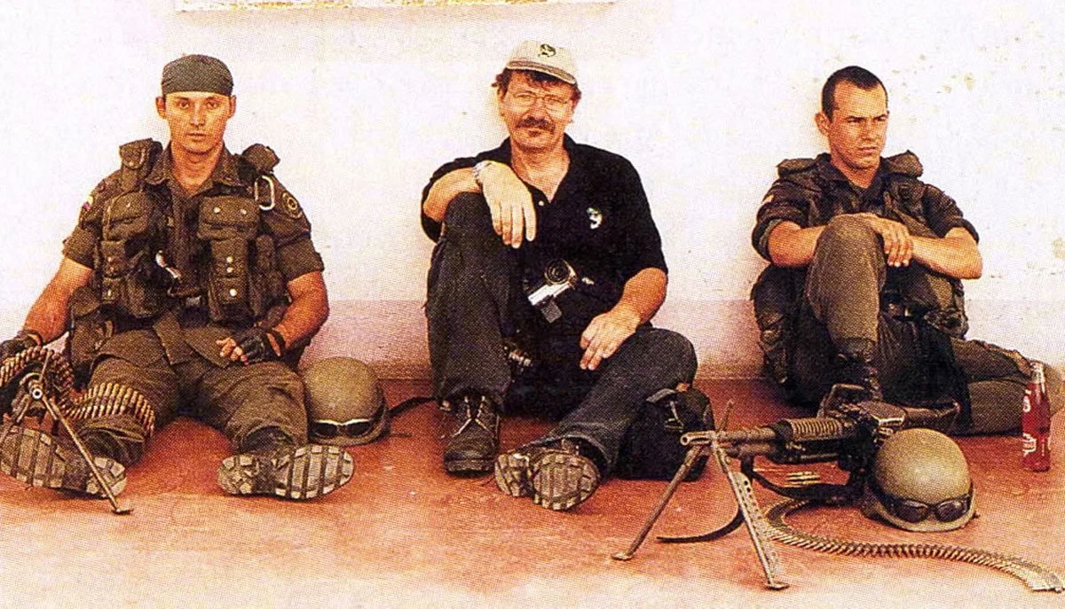 Three men sitting on the floor, wearing military and tactical gear, with helmets, sunglasses, and firearms.
