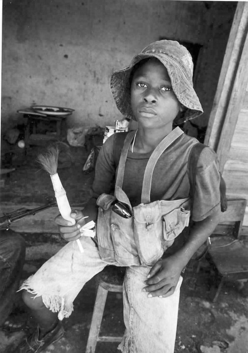 Member of the Small Boys Unit in Vonjoma, Liberia, during the civil war. He is carrying a controller that he insists moves bullets away from him. ©RYP, all rights reserved