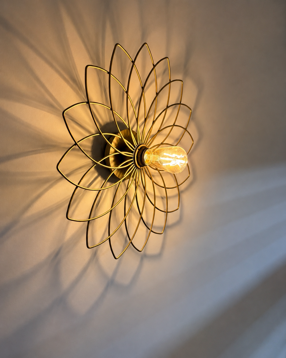 Lampe moderne en forme de fleur en fil métallique doré, éclairée, projetant des ombres au mur.