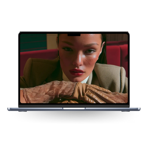 Close-up of a woman with dark hair and makeup, resting her head on her arms, sitting behind a laptop with a screen showing her face.