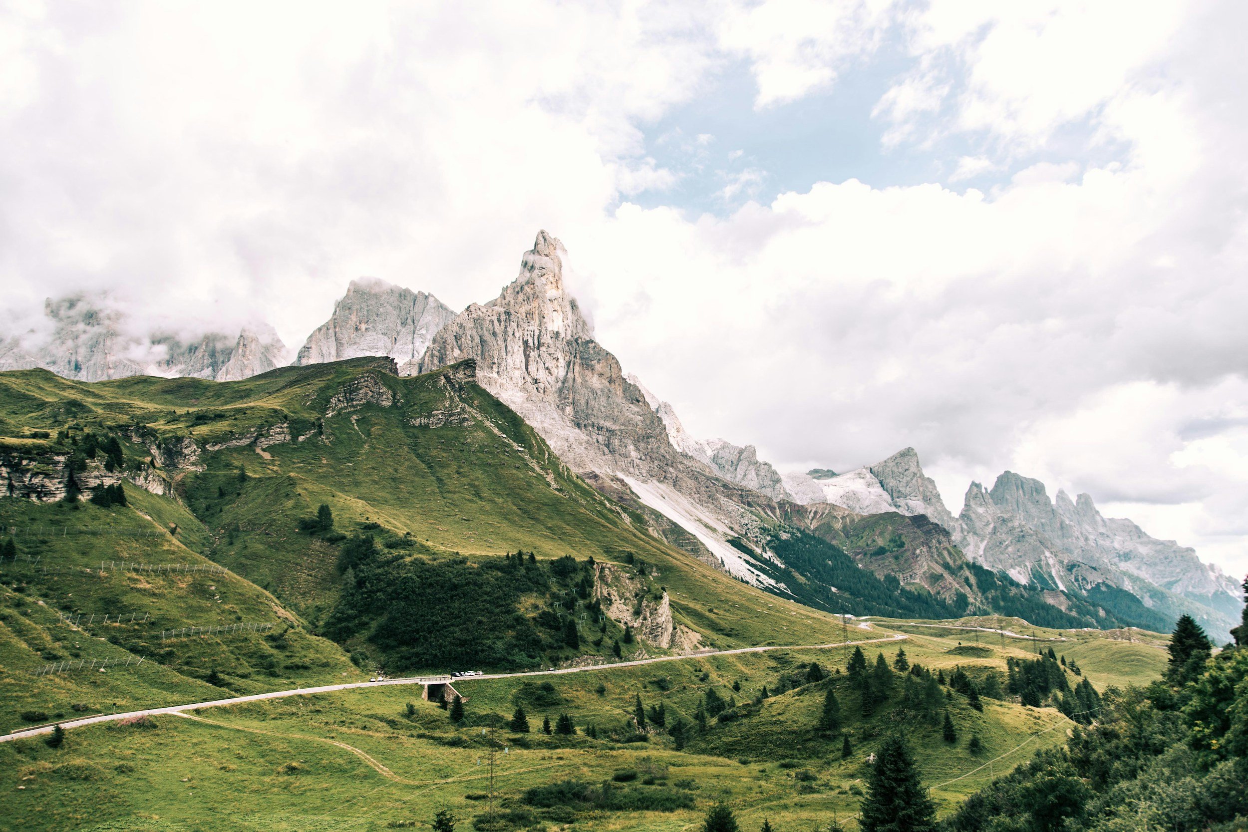 Scenic mountain landscape with green hills, rocky peaks, and partly cloudy sky.