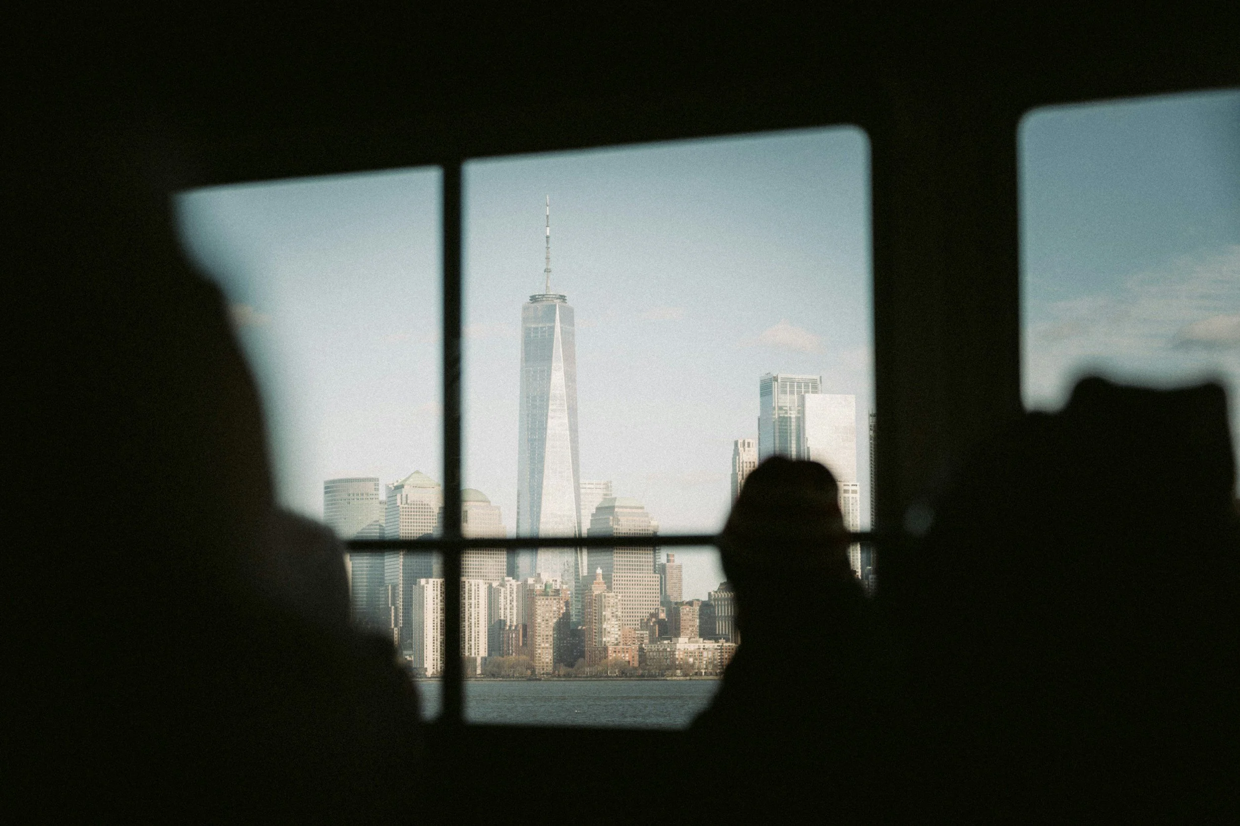 View of a city skyline through a window with dark framing, featuring One World Trade Center in New York City.