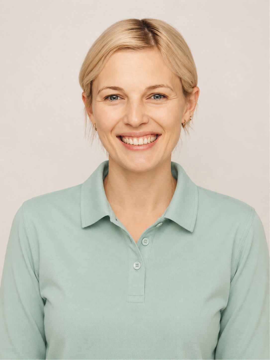 Nahaufnahme eines lachenden blonden Frau in einem grünen Polo-Shirt vor neutralem Hintergrund.
