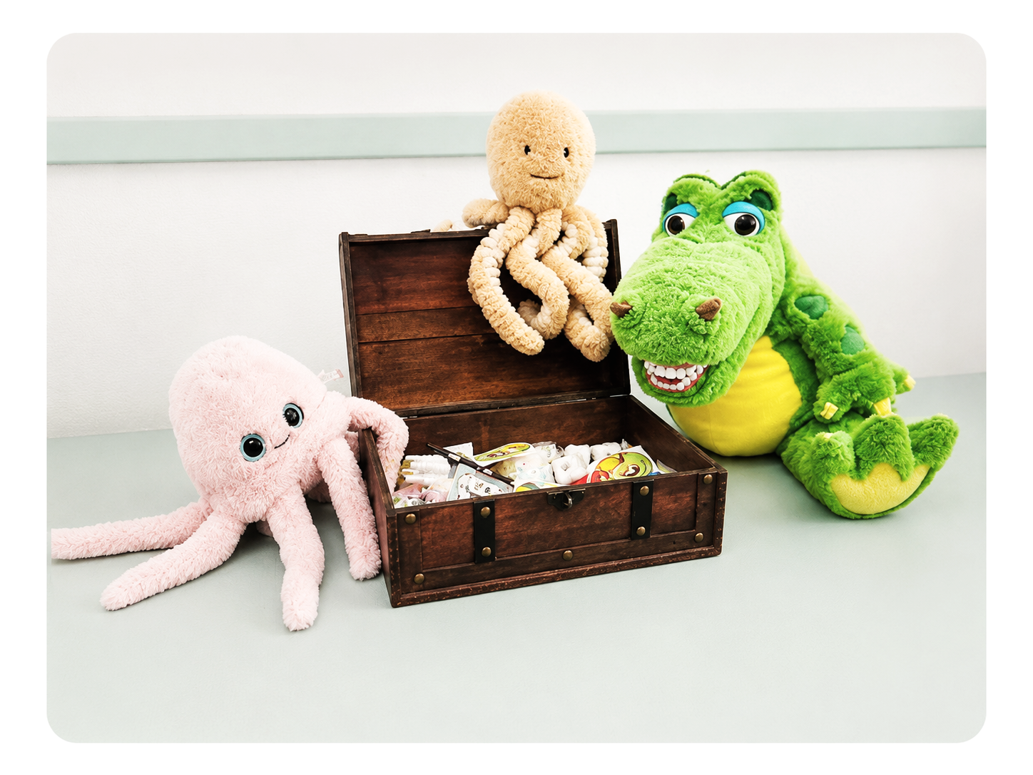 Plüschtiere eines pinken Tieres, eines braunen Oktopus und eines grünen Krokodils, die um eine offene Holzkiste mit Medikamenten herum sitzen.