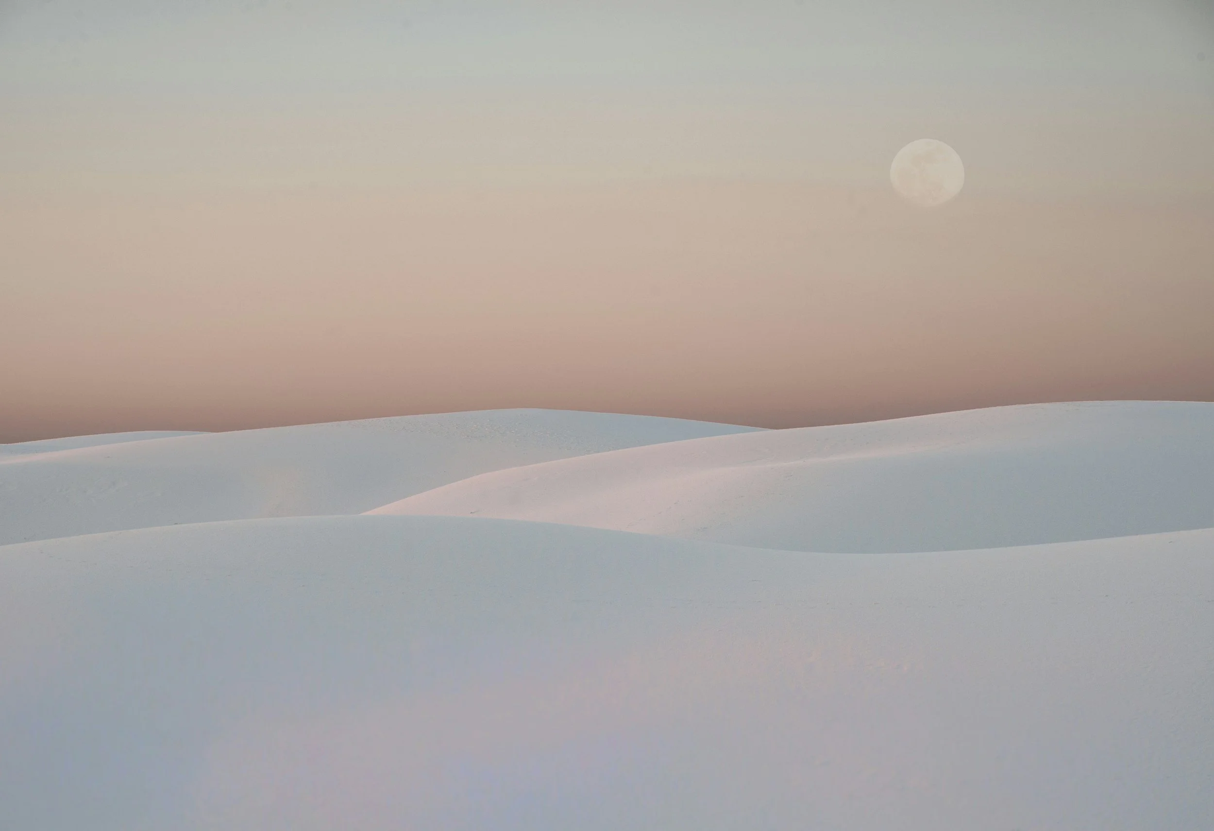Snow-covered hills under a pastel pink and blue sky with a visible moon.