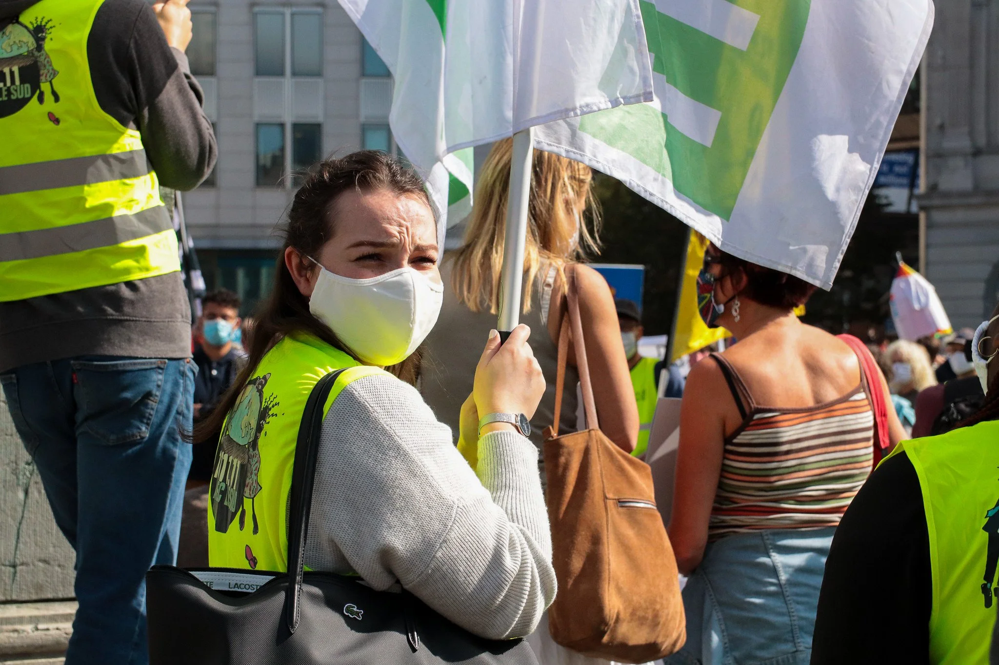 People wearing yellow safety vests and masks gathered outdoors during a protest or demonstration, with some holding flags.