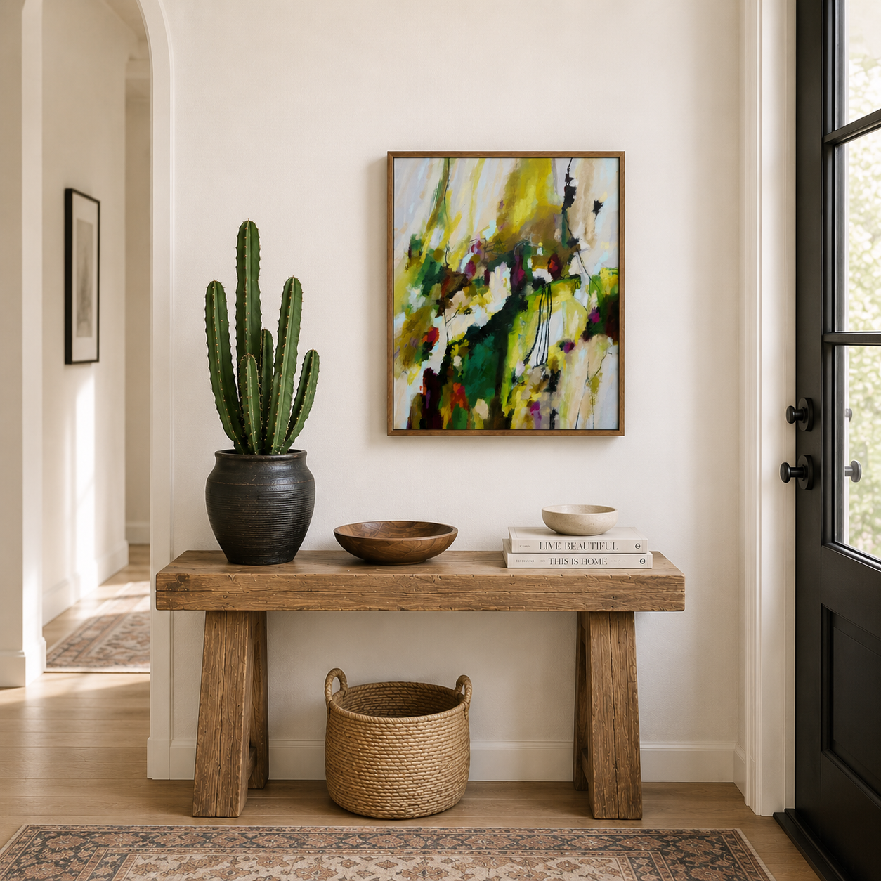 Entryway with a wooden console table, decorative bowls, a potted cactus, a basket beneath, abstract painting on the wall by Brita Nordin, and books, near a window and doorway.