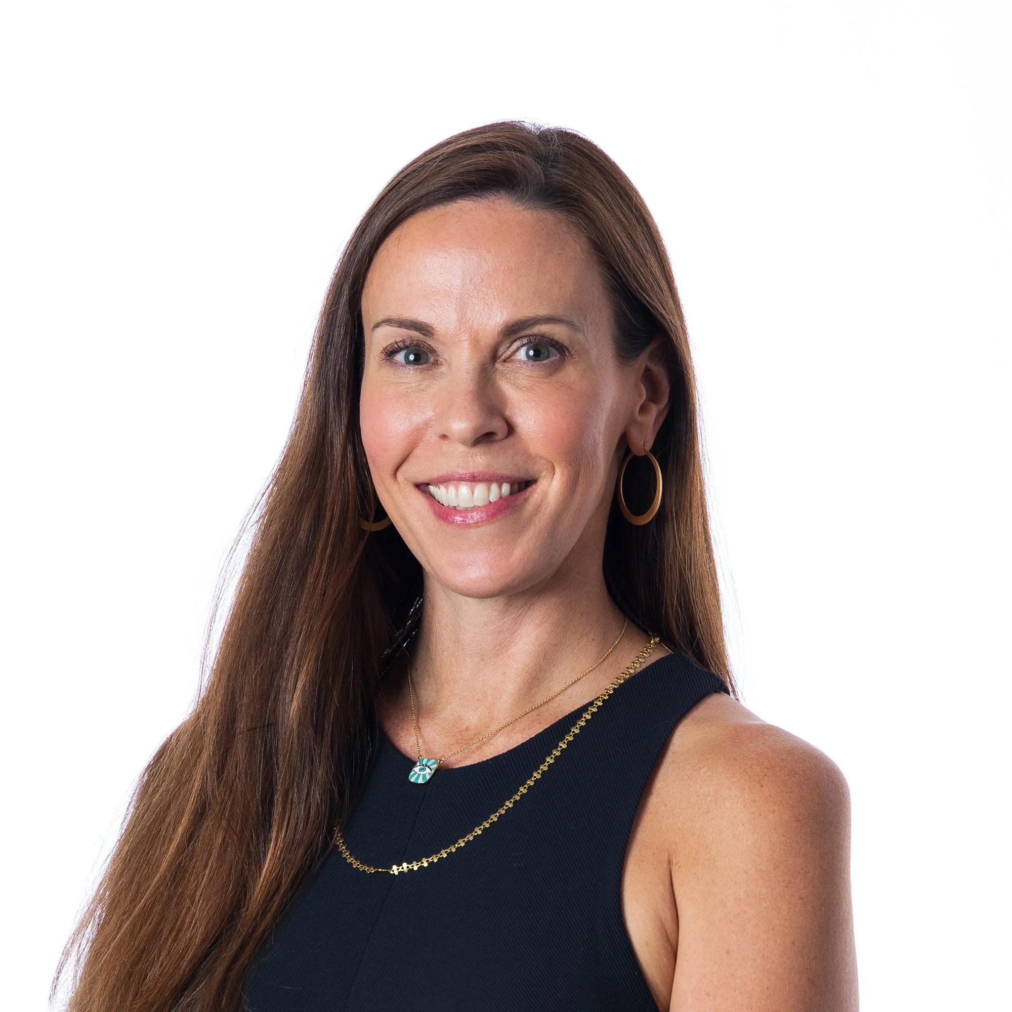 Close-up of Brita Nordin, a woman with long brown hair, blue eyes, and hoop earrings, wearing a black top and gold jewelry, smiling against a white background.