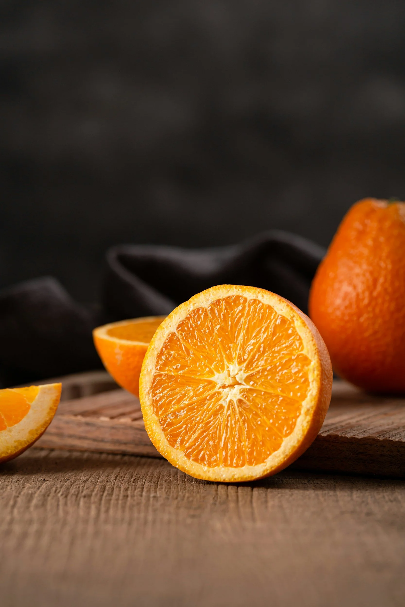 Close-up of fresh sliced oranges on a wooden surface with a dark background.
