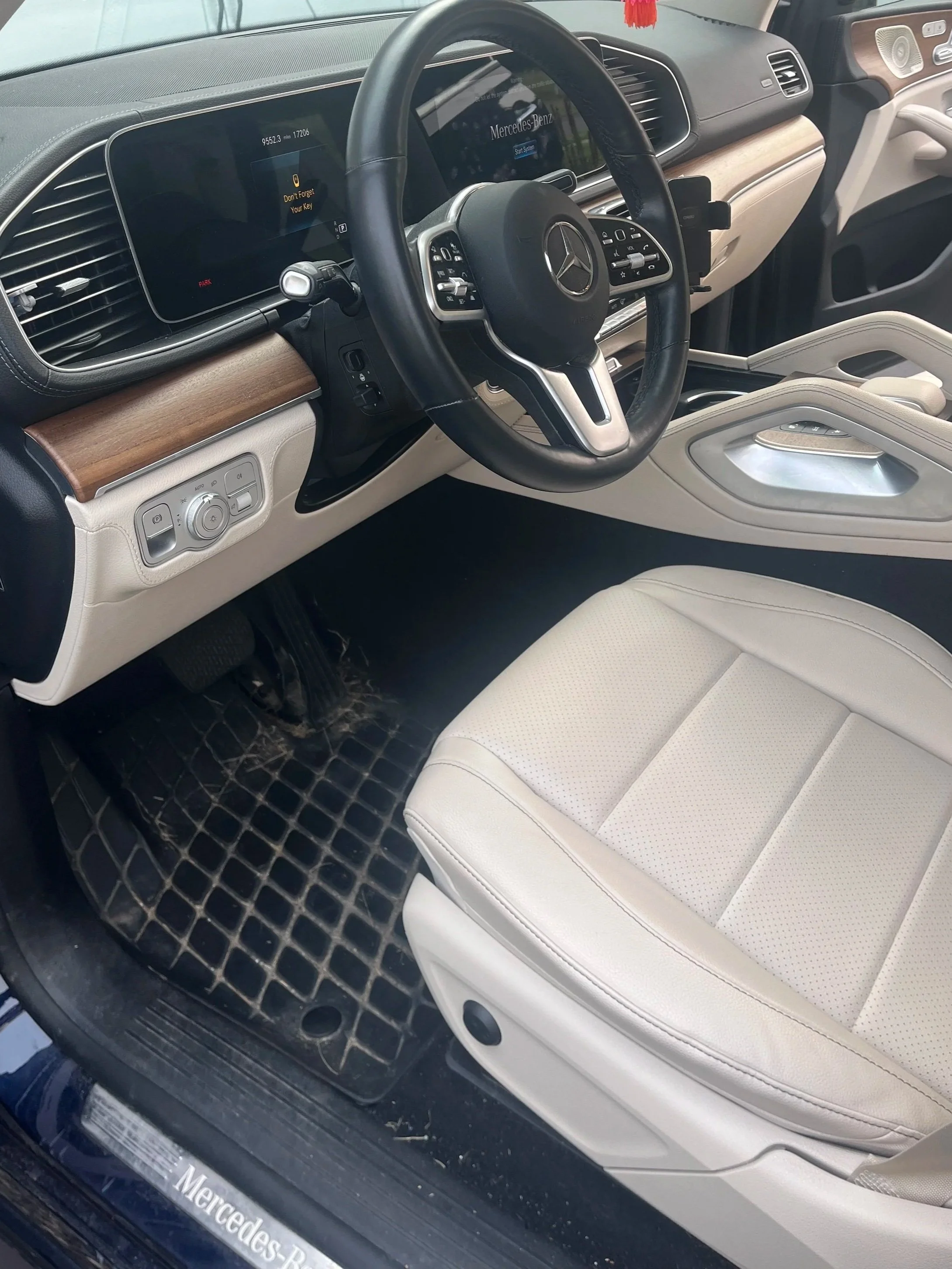 Interior of a Mercedes-Benz vehicle showing the dashboard, steering wheel, and front passenger seat. The dashboard has a modern digital display, and the interior features light-colored leather upholstery, wood trim, and control buttons near the seat and steering wheel.