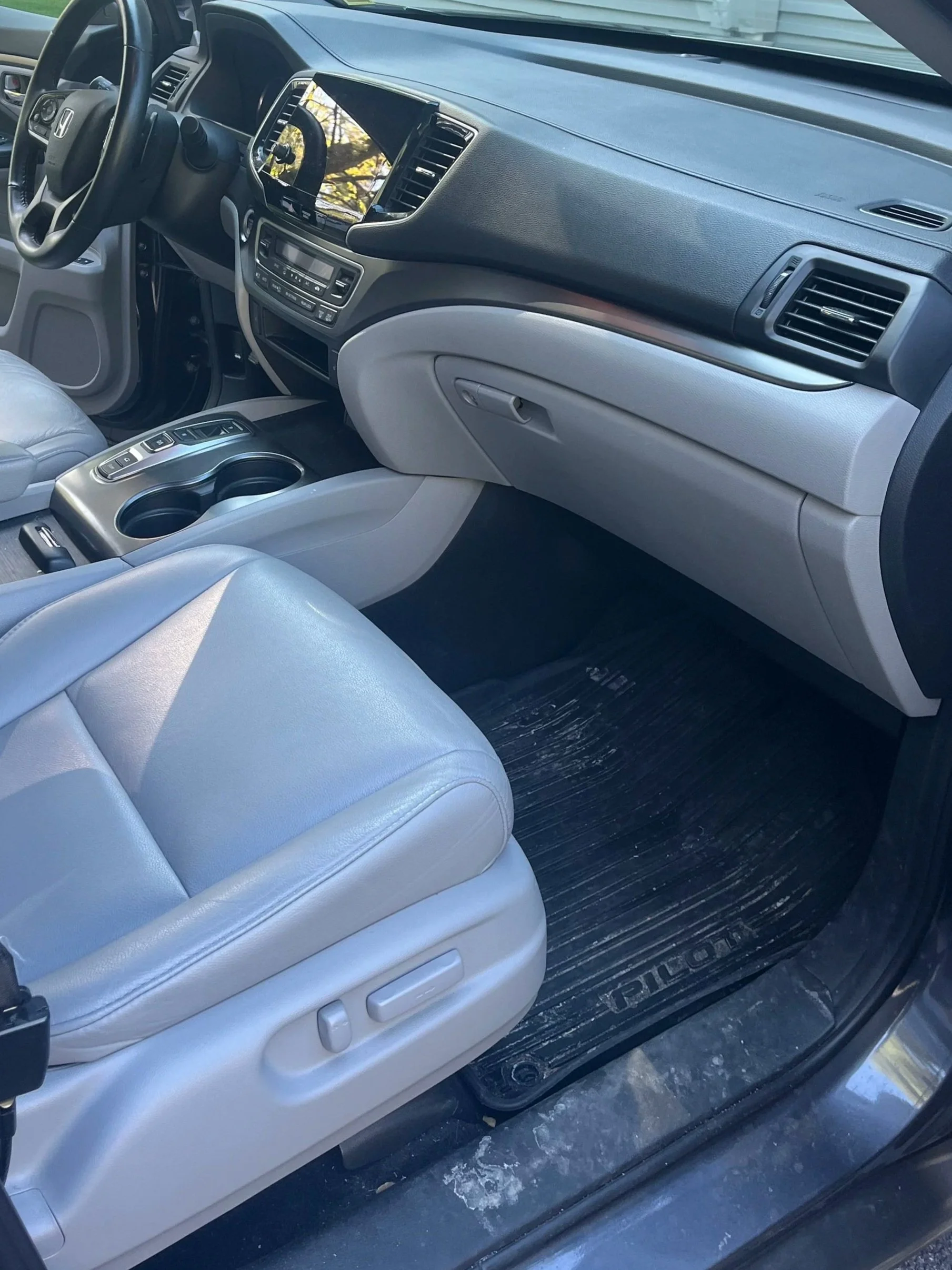 Inside of a vehicle showing the front passenger seat, dashboard, steering wheel, and center console with cup holders.