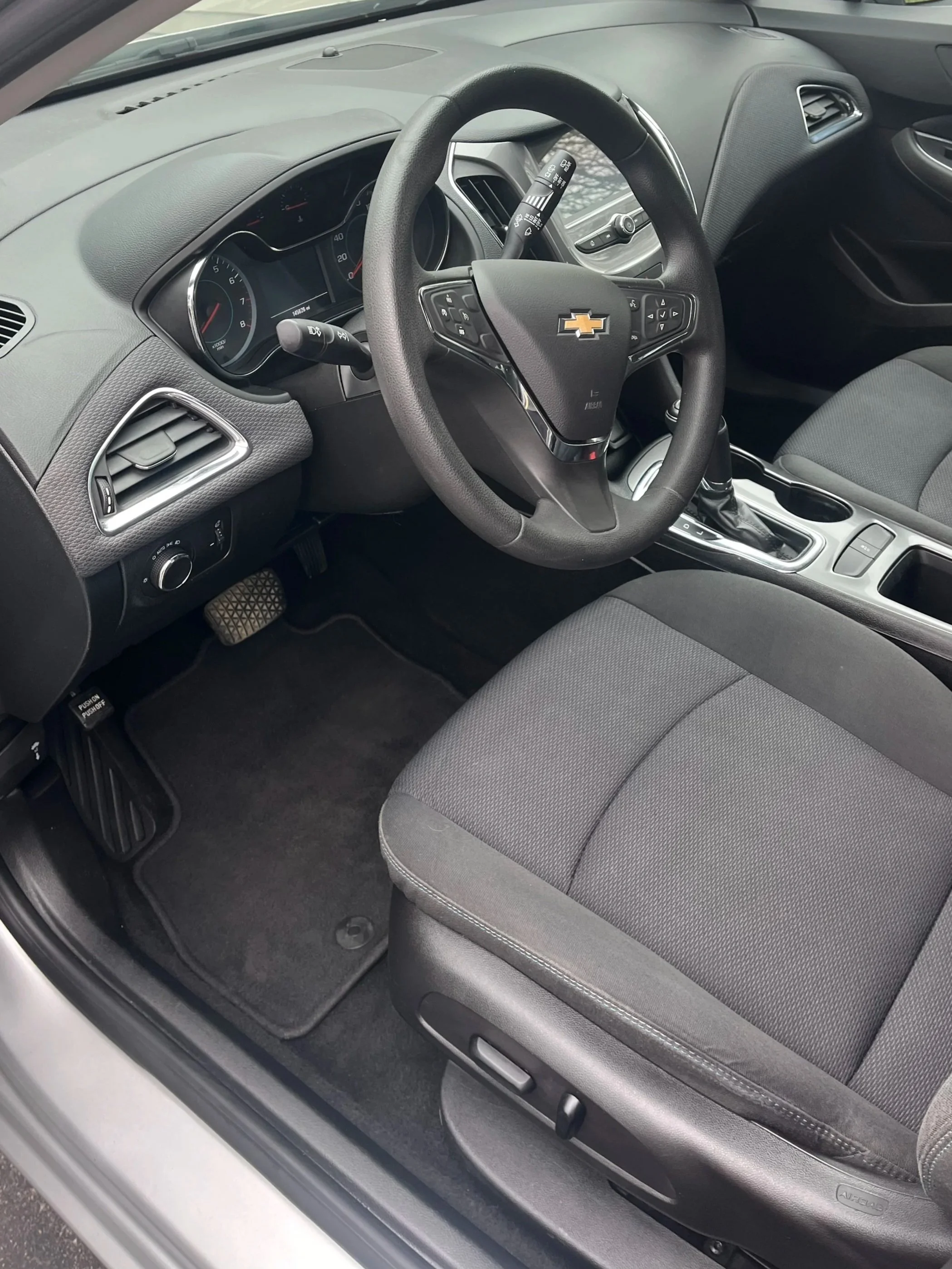 Inside the front passenger side of a Chevrolet vehicle, showing the dashboard, steering wheel with Chevrolet emblem, gear shift, and gray car seat.