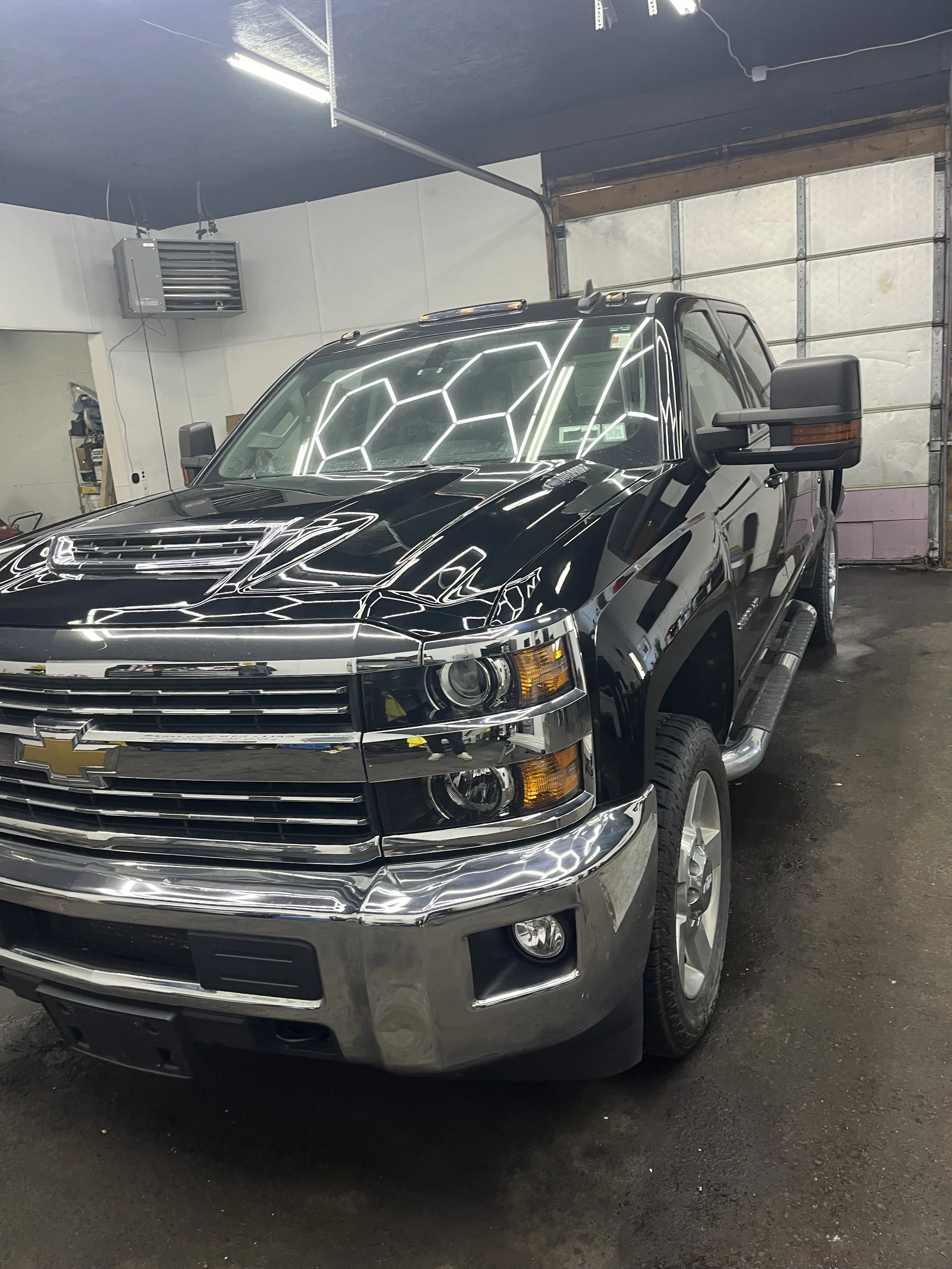 A black and chrome Chevrolet Silverado pickup truck parked inside a garage with a closed garage door and fluorescent lights reflecting on its surface.