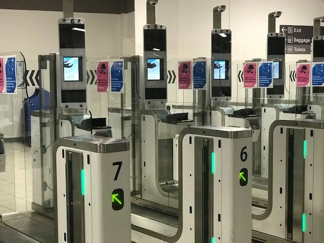 Airport security eGates lined up at the security checkpoint with green arrows indicating open lanes.